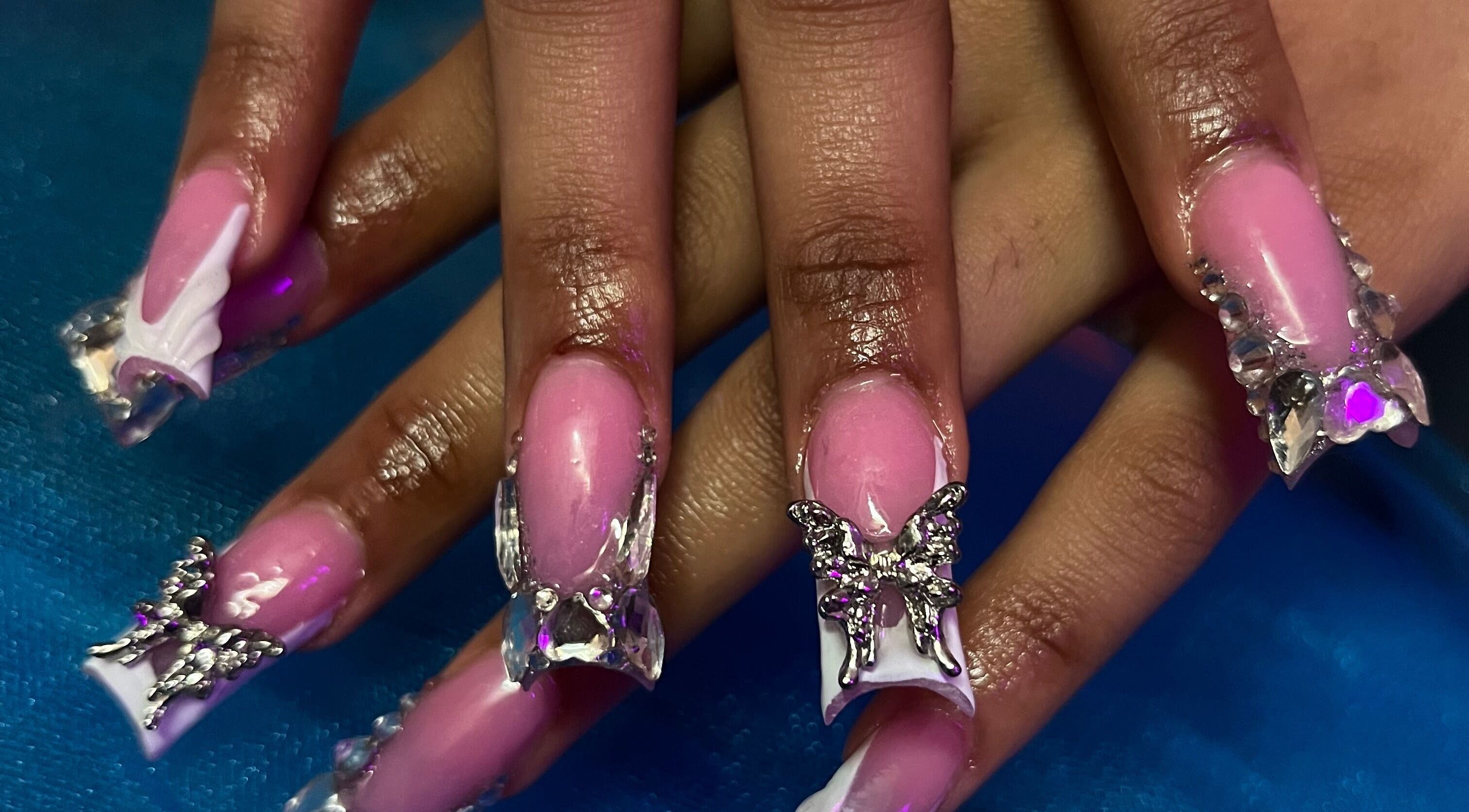 Elegant butterfly nail art at Visage VERITAS in Troy, New York, US features pink polish and crystal accents.