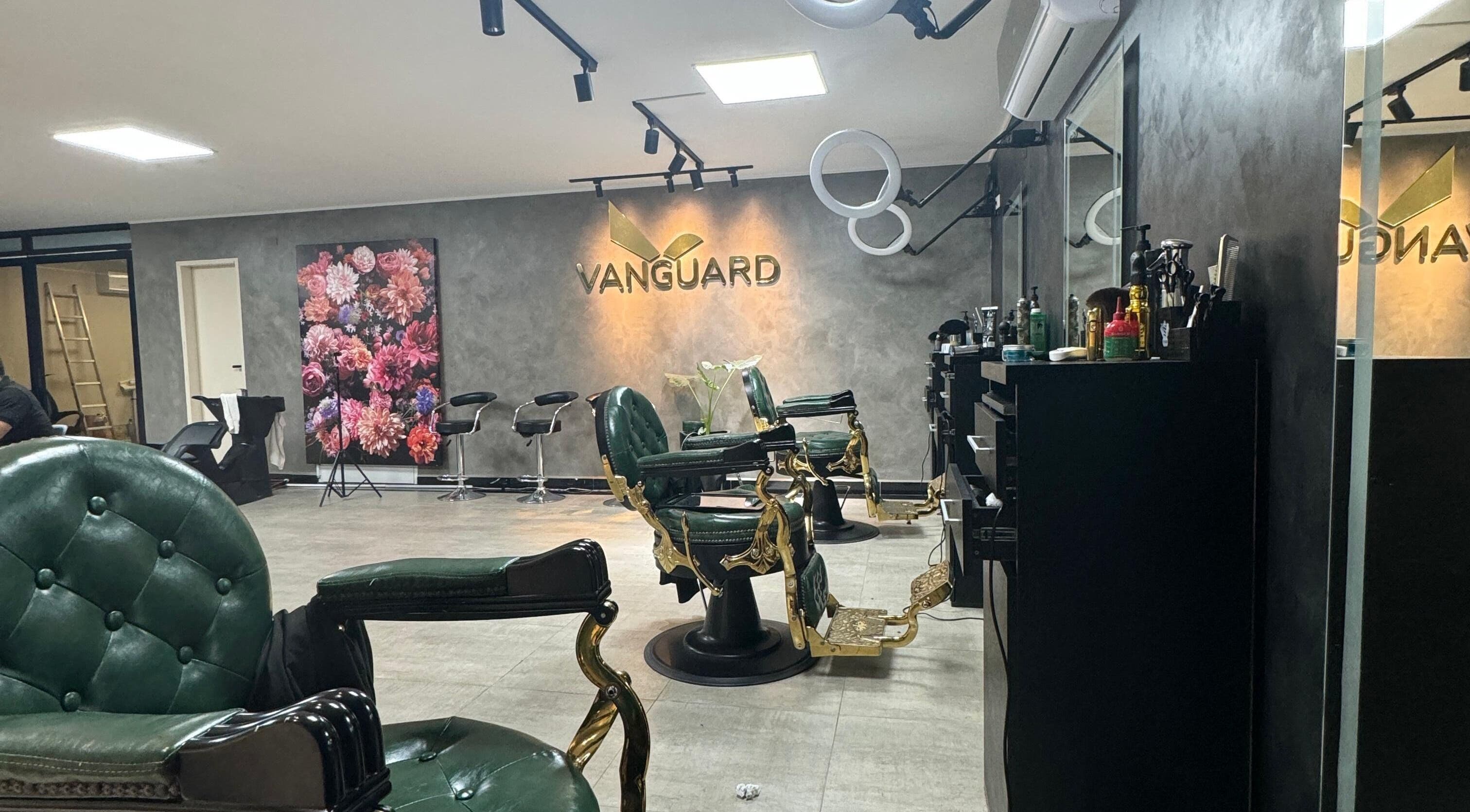 Interior elegante de VANGUARD en Santa Cruz De La Sierra, con sillas de barbero verdes y decoración floral.