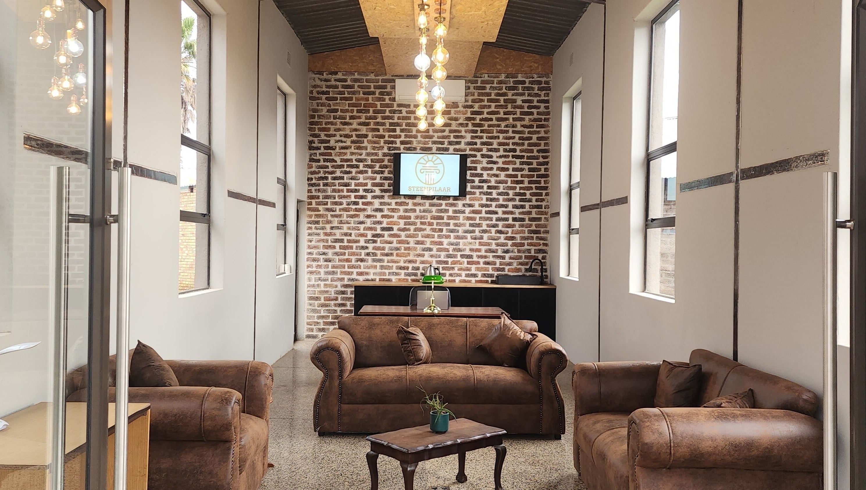 Cozy lounge at Steenpilaar, featuring leather sofas and a brick wall, located in Nigel, Gauteng, ZA.