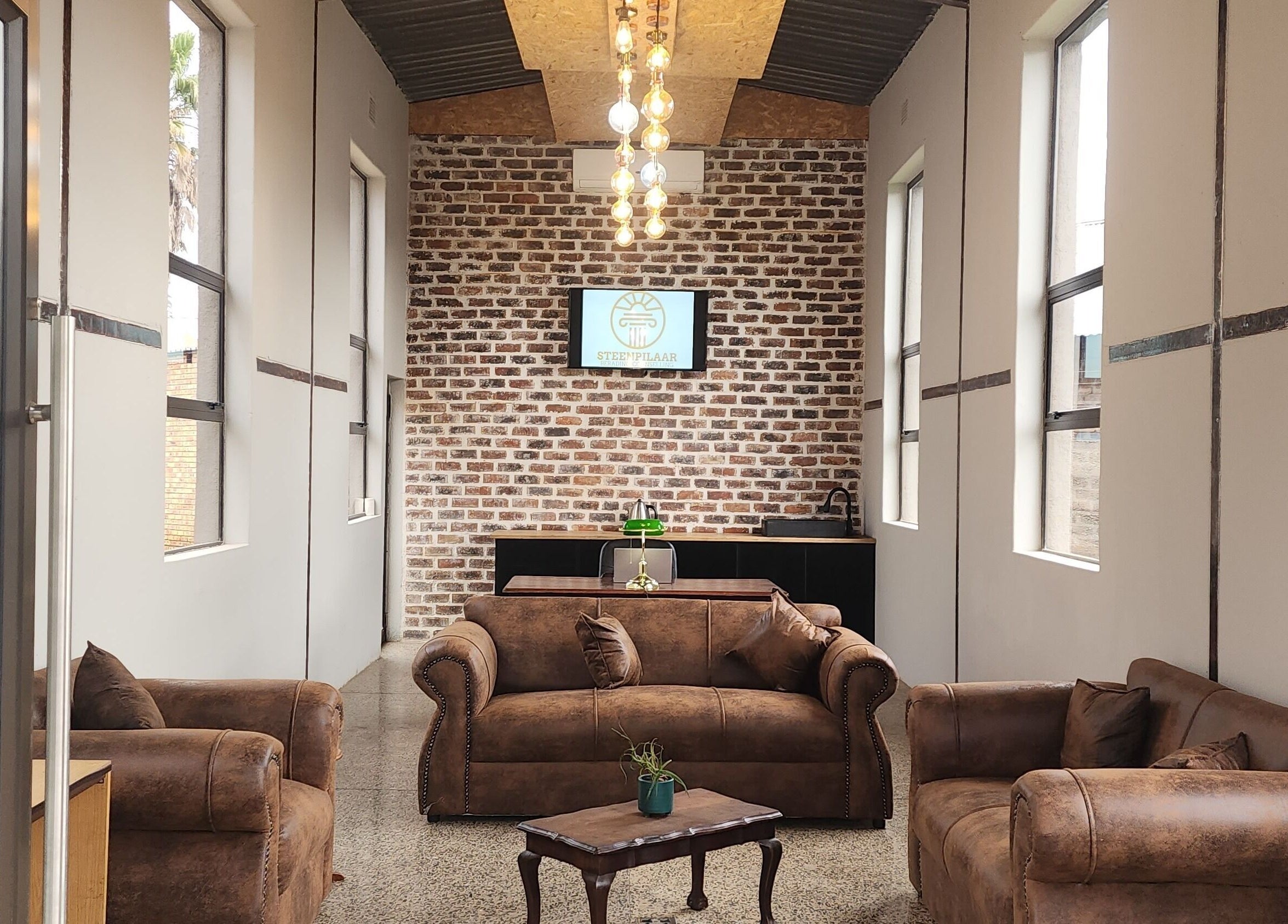 Cozy lounge at Steenpilaar, featuring leather sofas and a brick wall, located in Nigel, Gauteng, ZA.