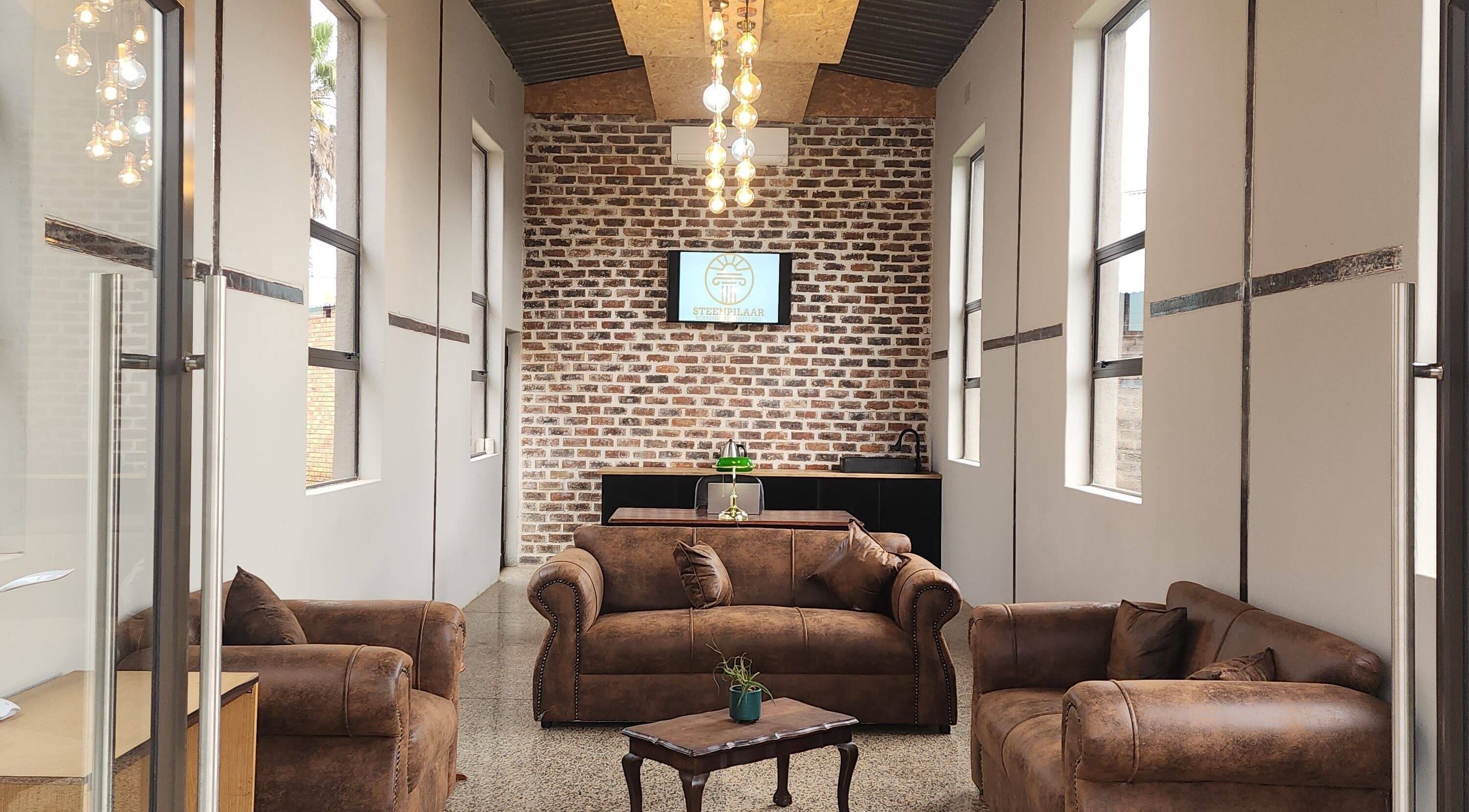 Cozy lounge at Steenpilaar, featuring leather sofas and a brick wall, located in Nigel, Gauteng, ZA.
