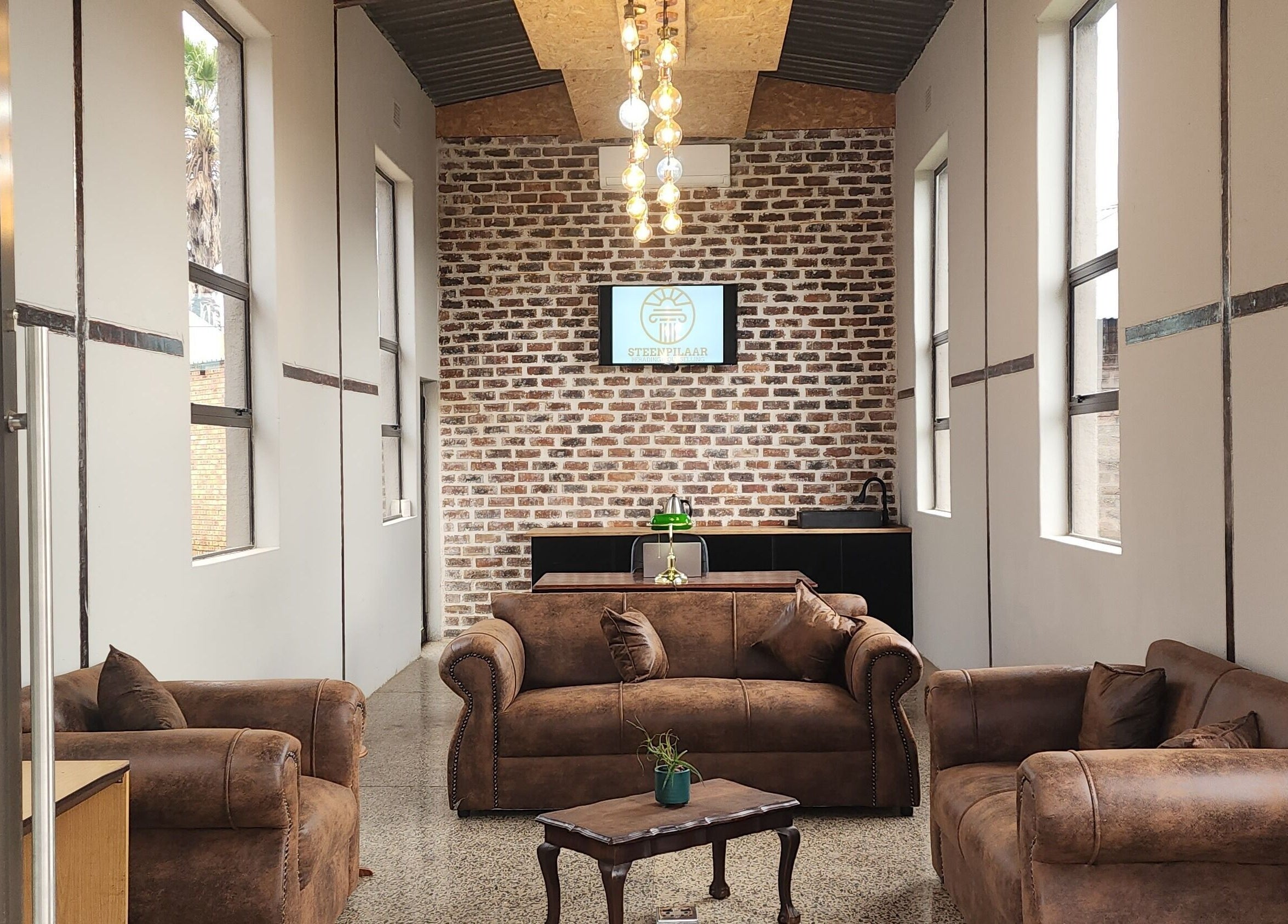 Elegant lounge at Steenpilaar, Nigel, Gauteng, ZA with brown sofas, brick wall, and modern lighting.