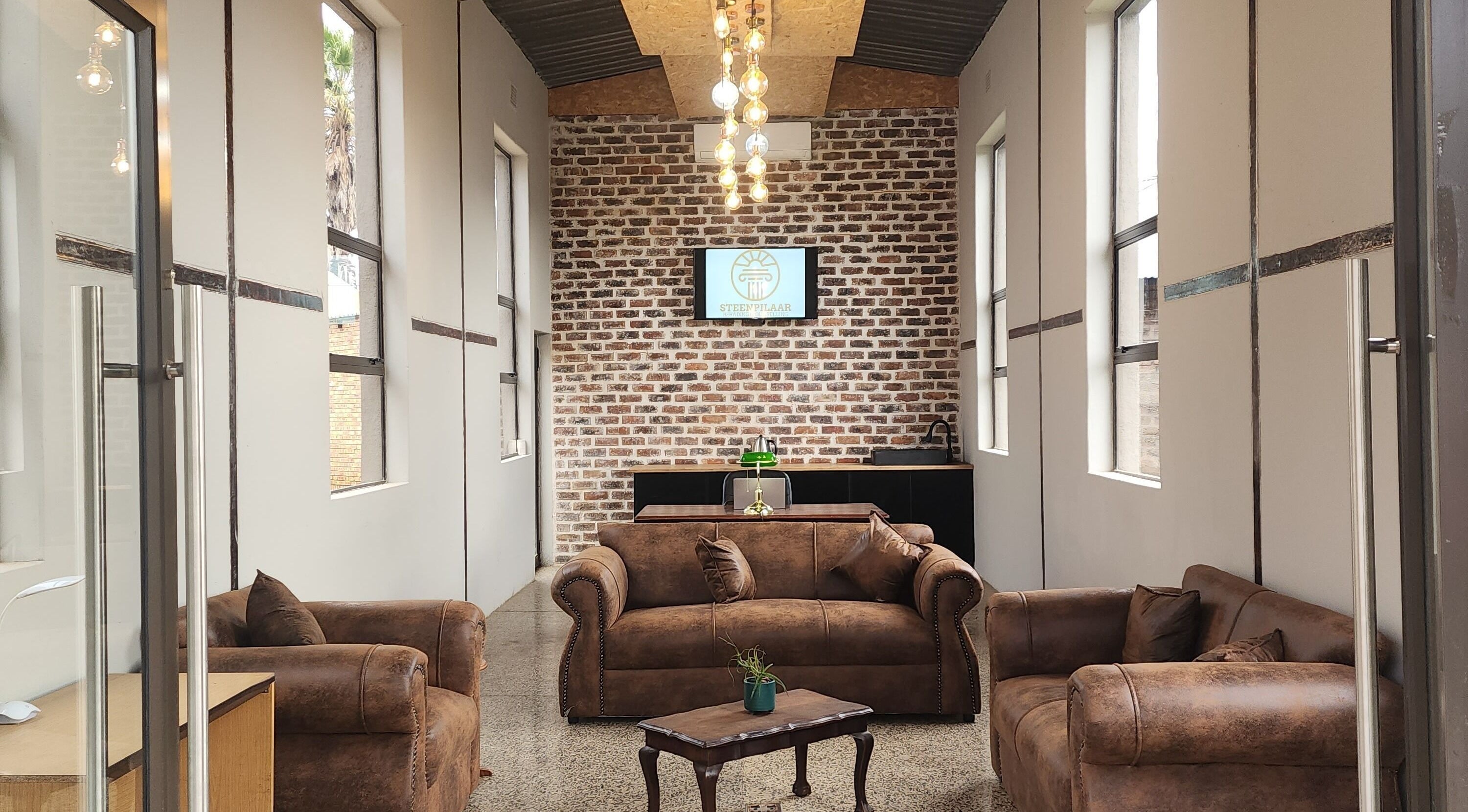 Elegant lounge at Steenpilaar, Nigel, Gauteng, ZA with brown sofas, brick wall, and modern lighting.
