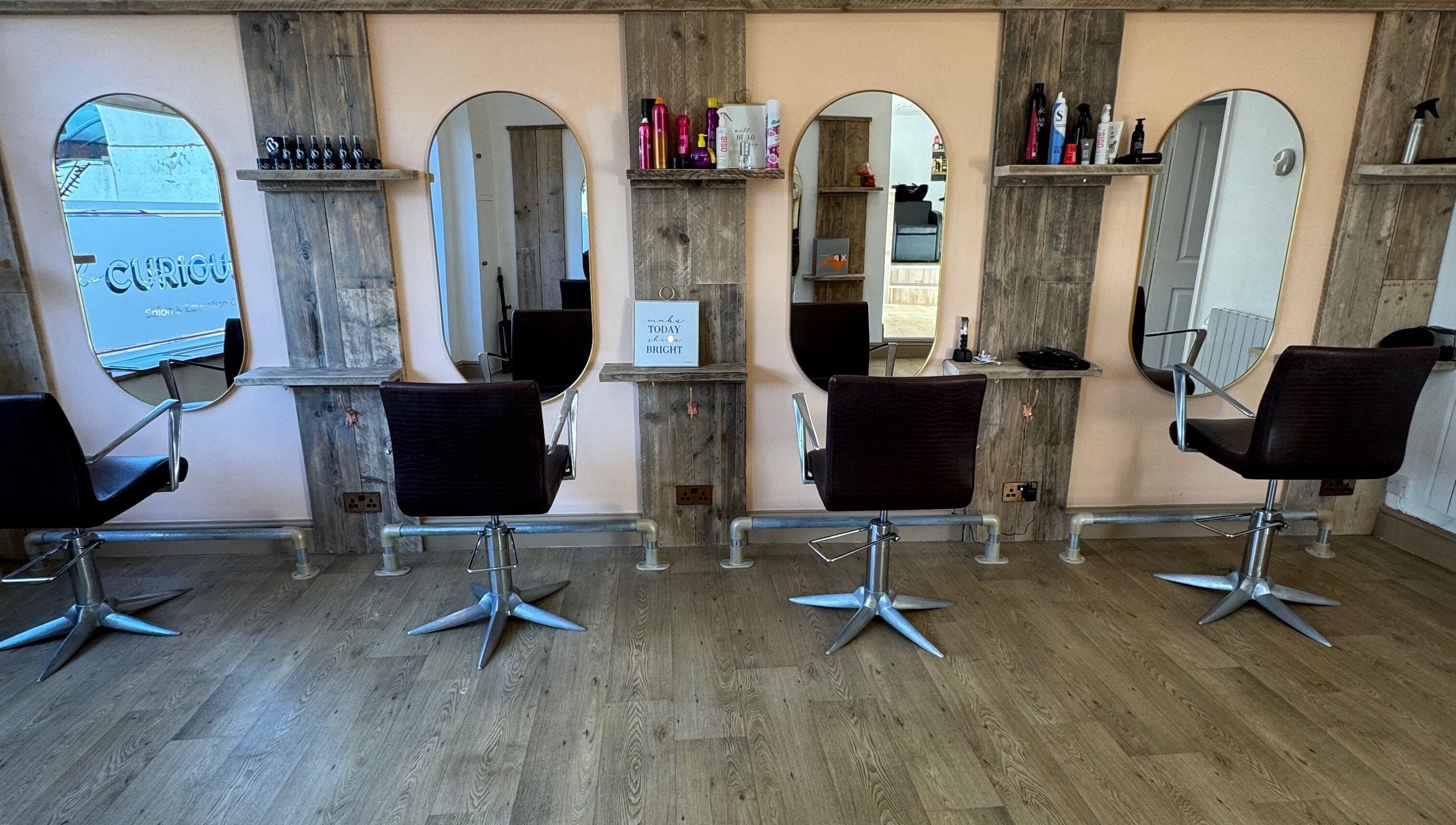 The Curious Stylist interior view in Bovey Tracey, England, GB showing four styling chairs and modern mirrors.