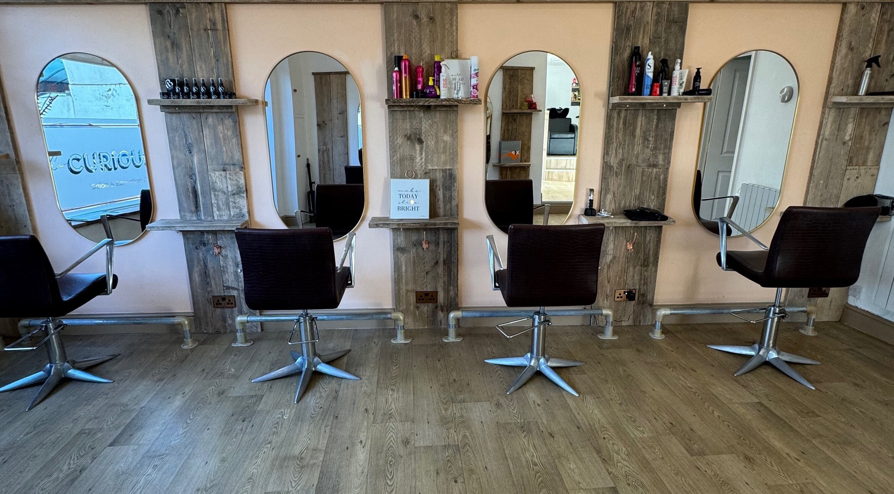 The Curious Stylist interior view in Bovey Tracey, England, GB showing four styling chairs and modern mirrors.