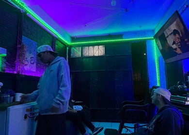 Interior moderno de Barber Studio Crisanto en Villa Nueva, Guatemala, GT, con iluminación neón y pantalla.