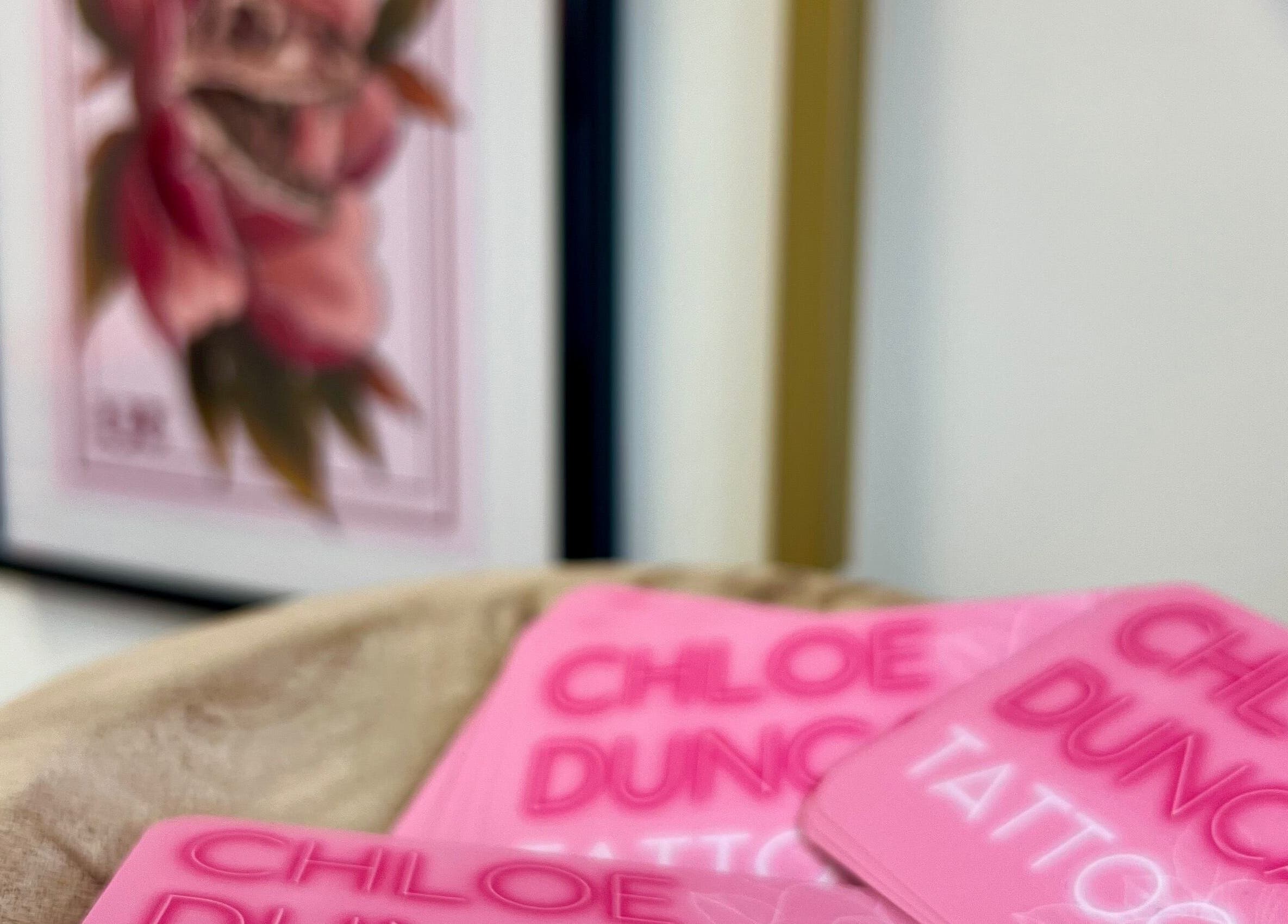 Chloe Duncan Tattoo cards on display at Rochester, England, GB, with floral artwork in the background.