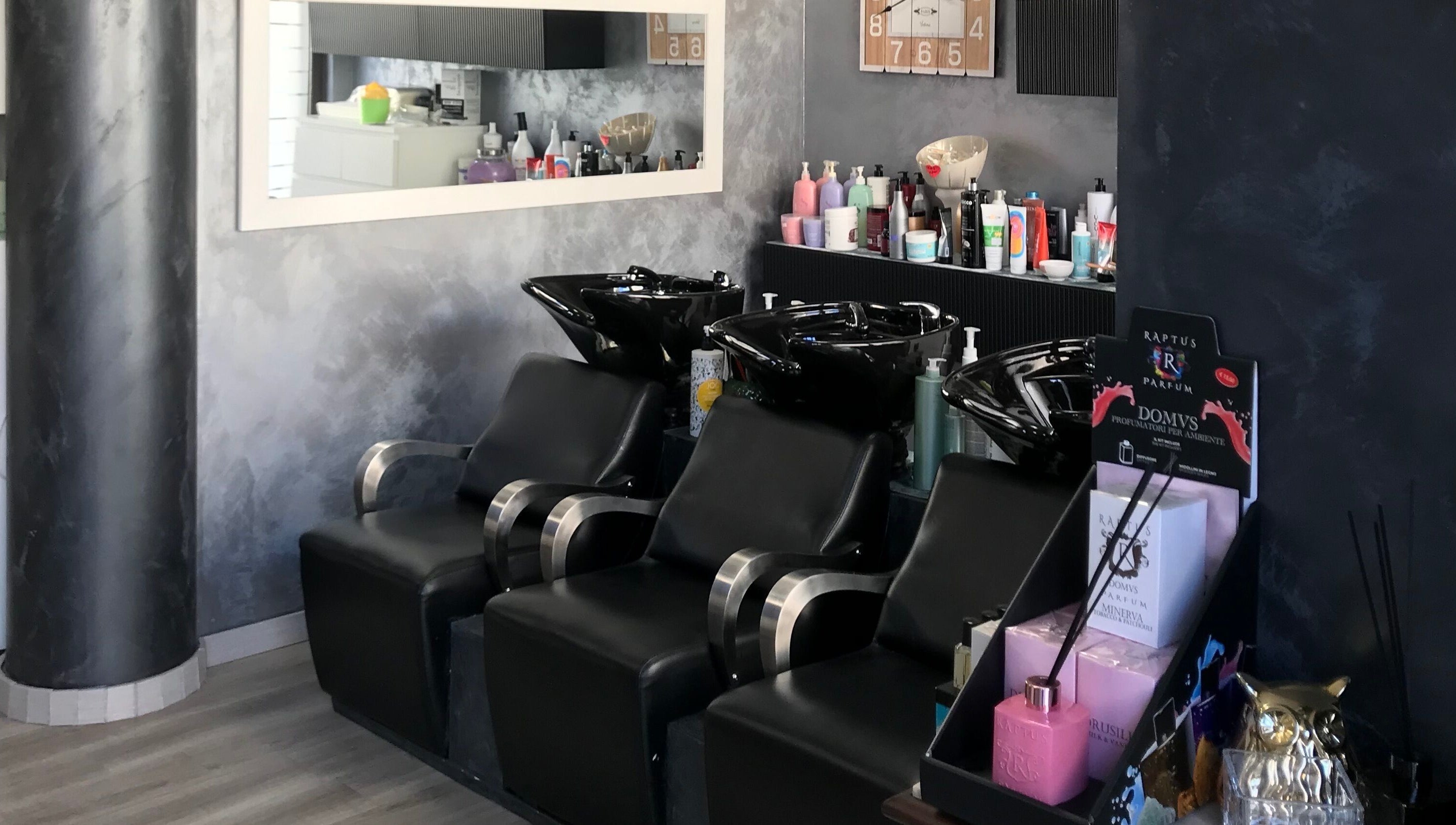 Zona lavaggio di Un Diavolo Per Capello a Brindisi, Puglia, IT con sedie nere e prodotti per capelli.