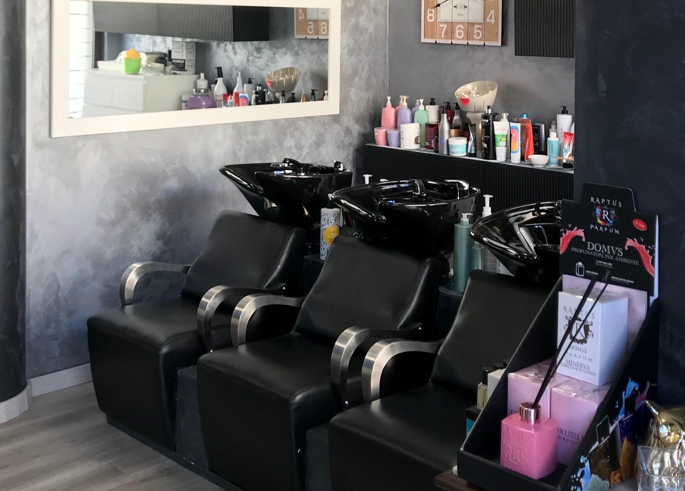 Zona lavaggio di Un Diavolo Per Capello a Brindisi, Puglia, IT con sedie nere e prodotti per capelli.