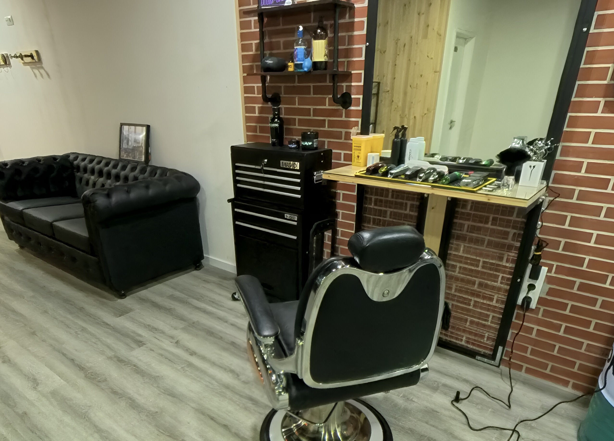 Interior da Paddock Barbershop ®️ em Lixa, Porto, PT, com cadeira de barbeiro e sofá elegante em preto.