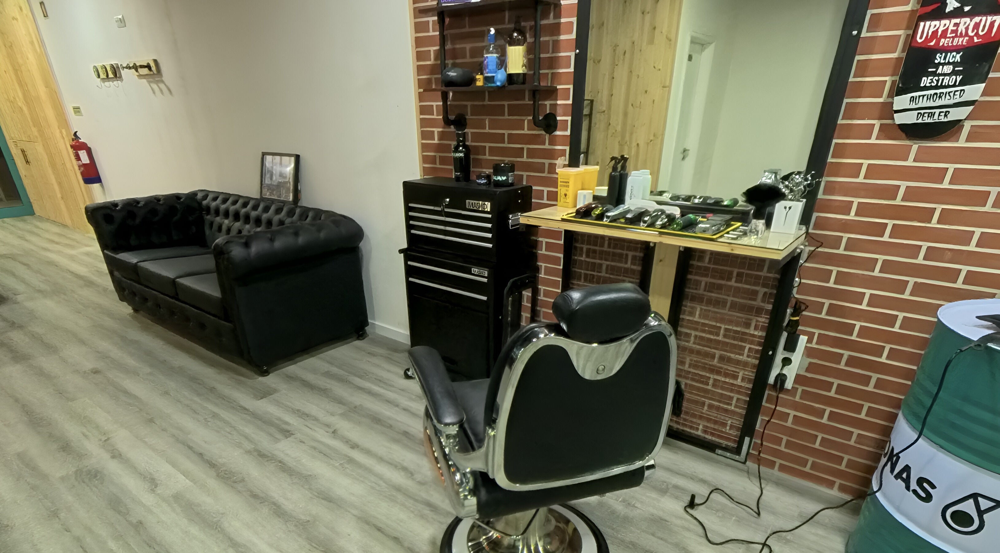 Interior da Paddock Barbershop ®️ em Lixa, Porto, PT, com cadeira de barbeiro e sofá elegante em preto.