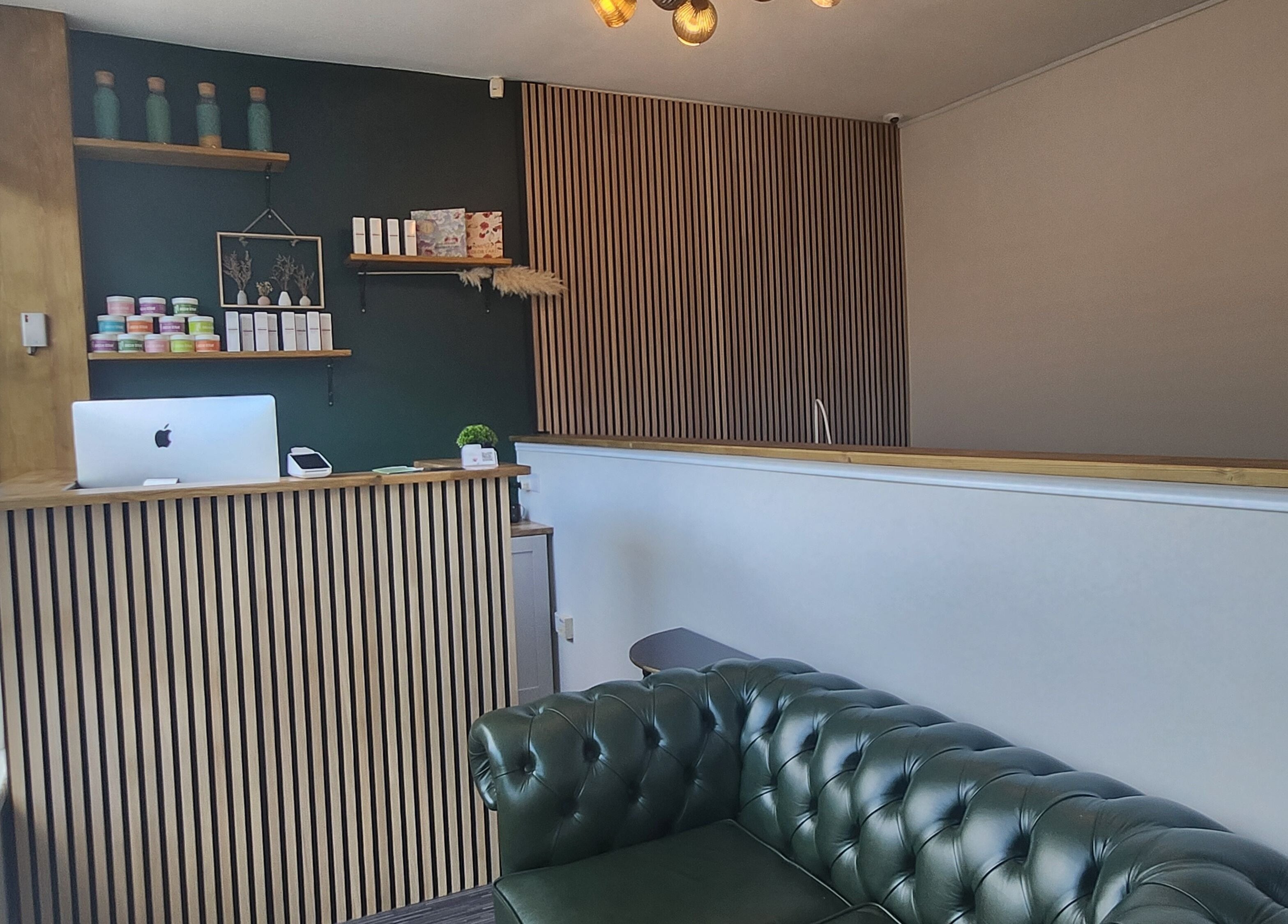 Elegant reception area at Next Level spa & beauty, Wallsend, England, GB with a modern green sofa and wooden counter.