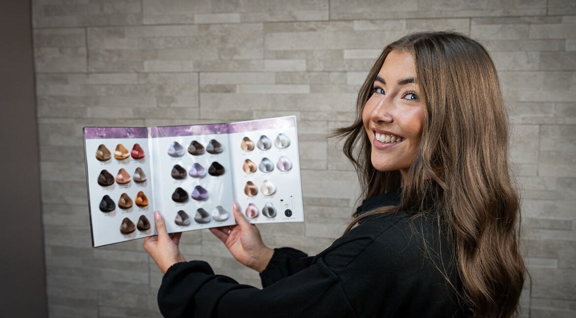 Stylist at AmberEliseHair in Ellon, Scotland, showcasing hair color options with a smile.