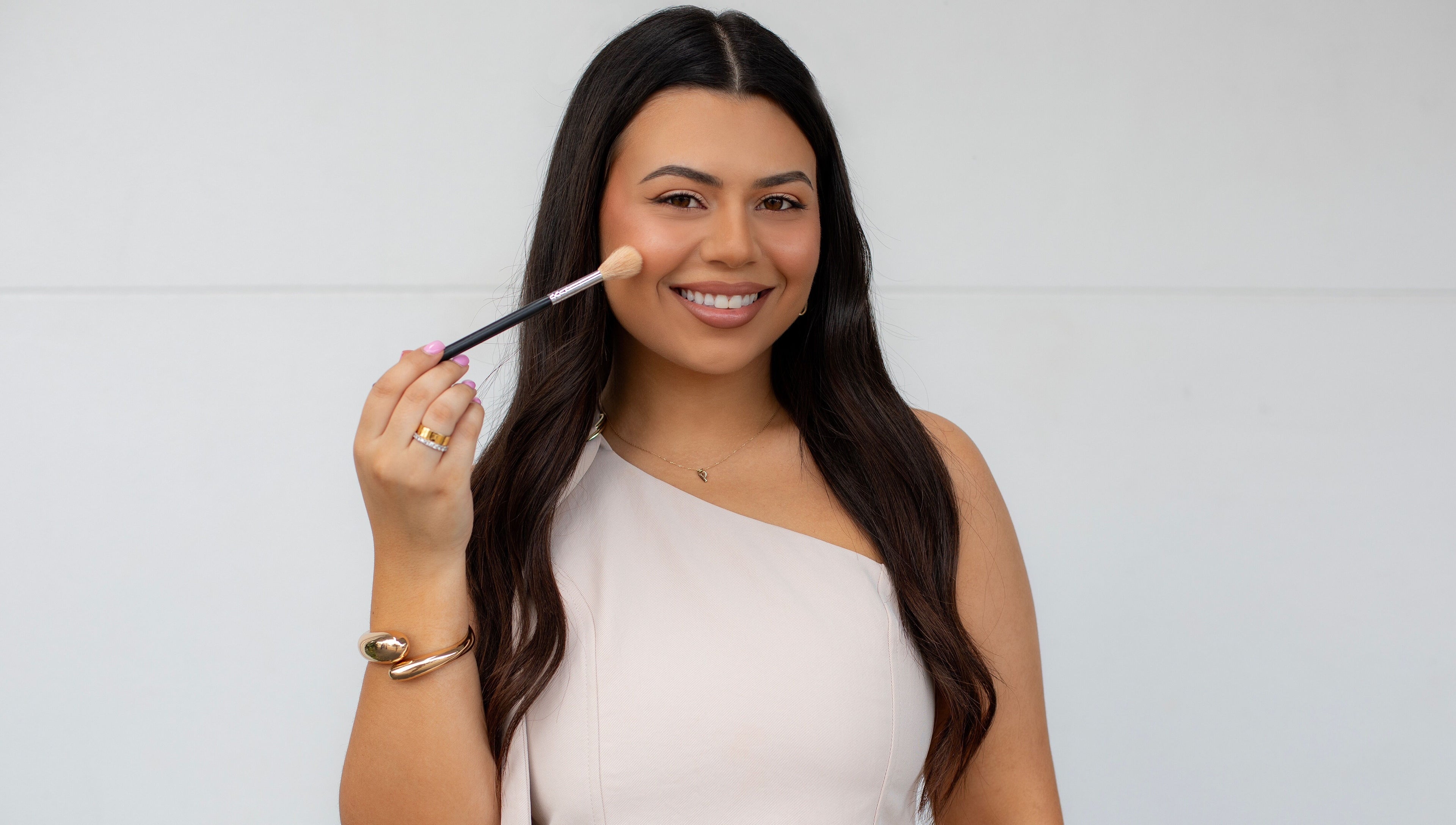 Smiling woman with makeup brush at By Paras, Carindale, Queensland, AU, showcasing beauty services.
