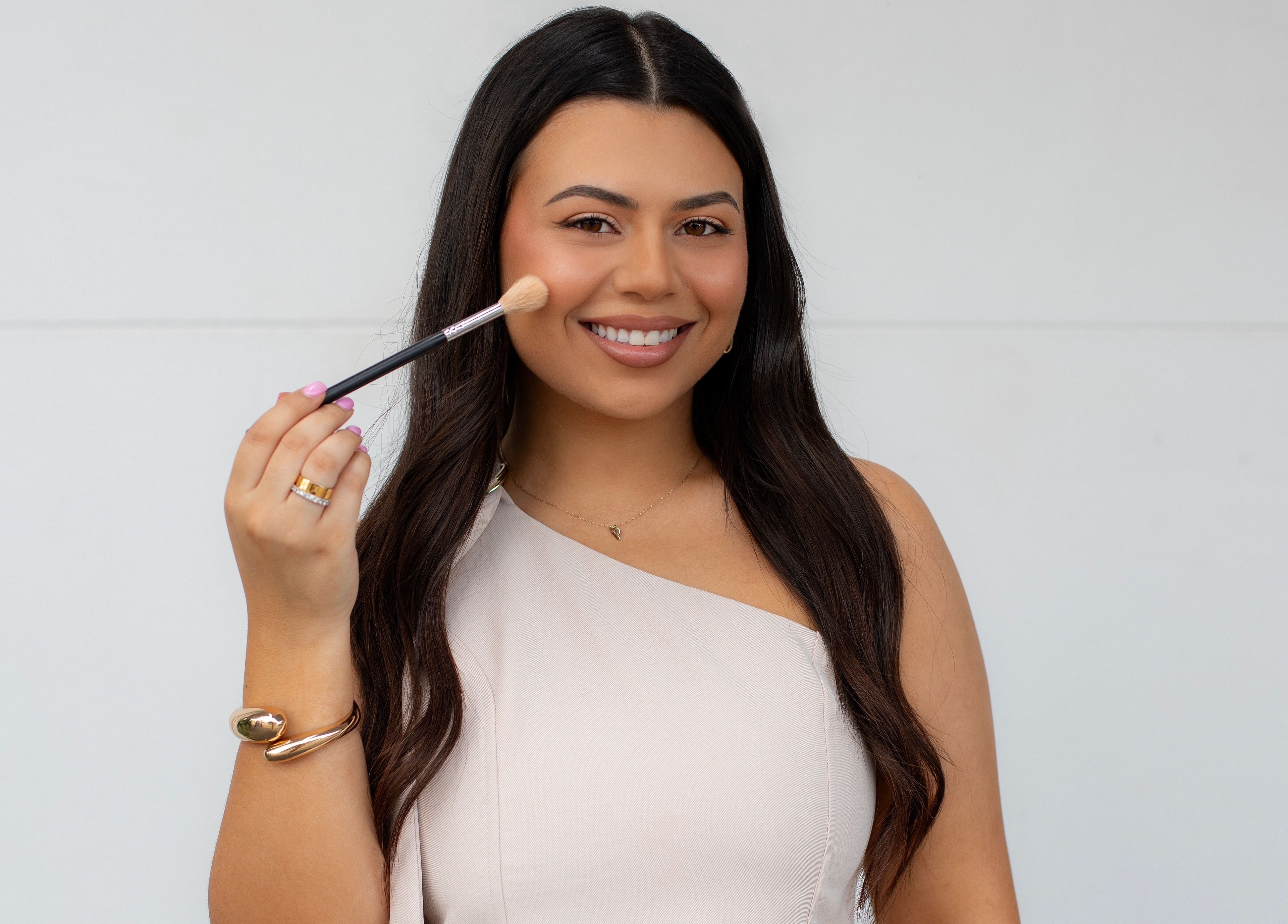Smiling woman with makeup brush at By Paras, Carindale, Queensland, AU, showcasing beauty services.