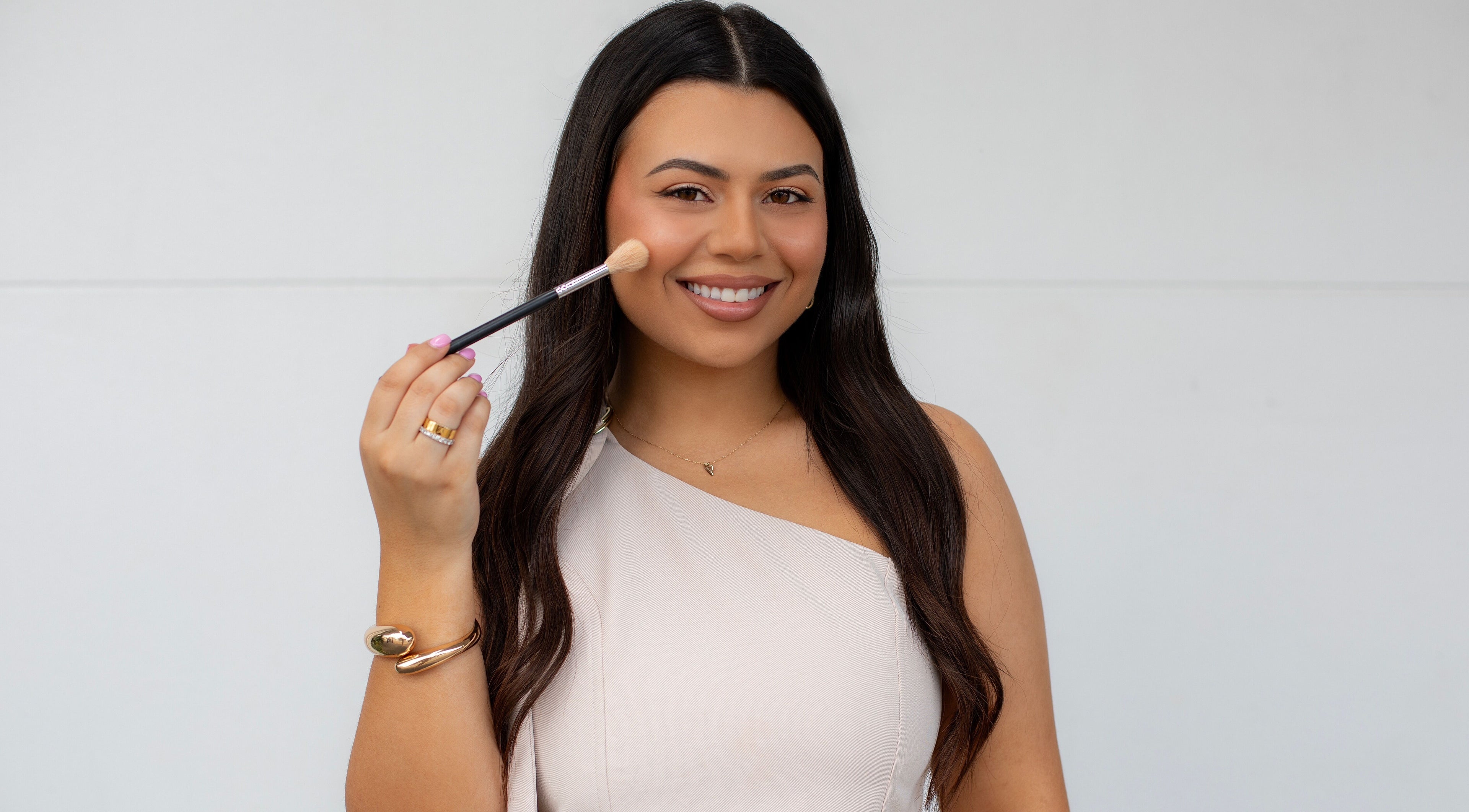 Smiling woman with makeup brush at By Paras, Carindale, Queensland, AU, showcasing beauty services.