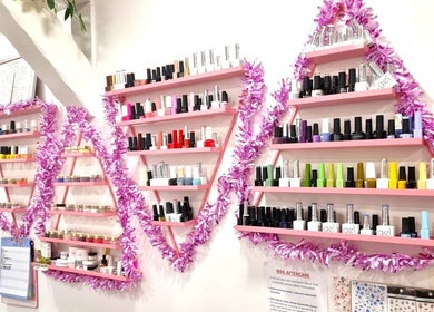 Vibrant nail polish shelves at Naiyah Nails, London, England, GB, adorned with pink garlands.