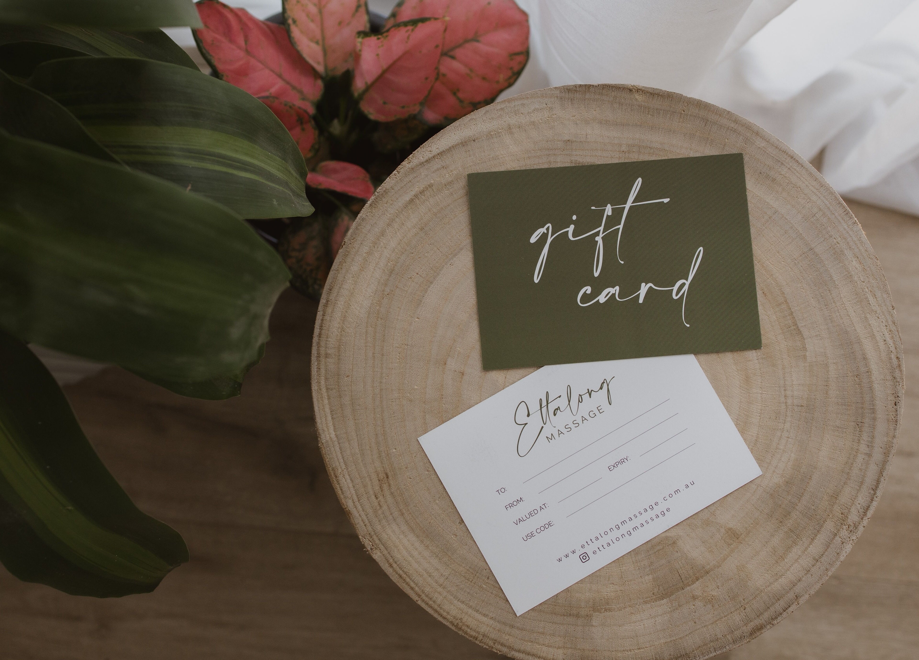 Ettalong Massage gift card on wooden table, Ettalong Beach, New South Wales, AU, surrounded by green leaves.