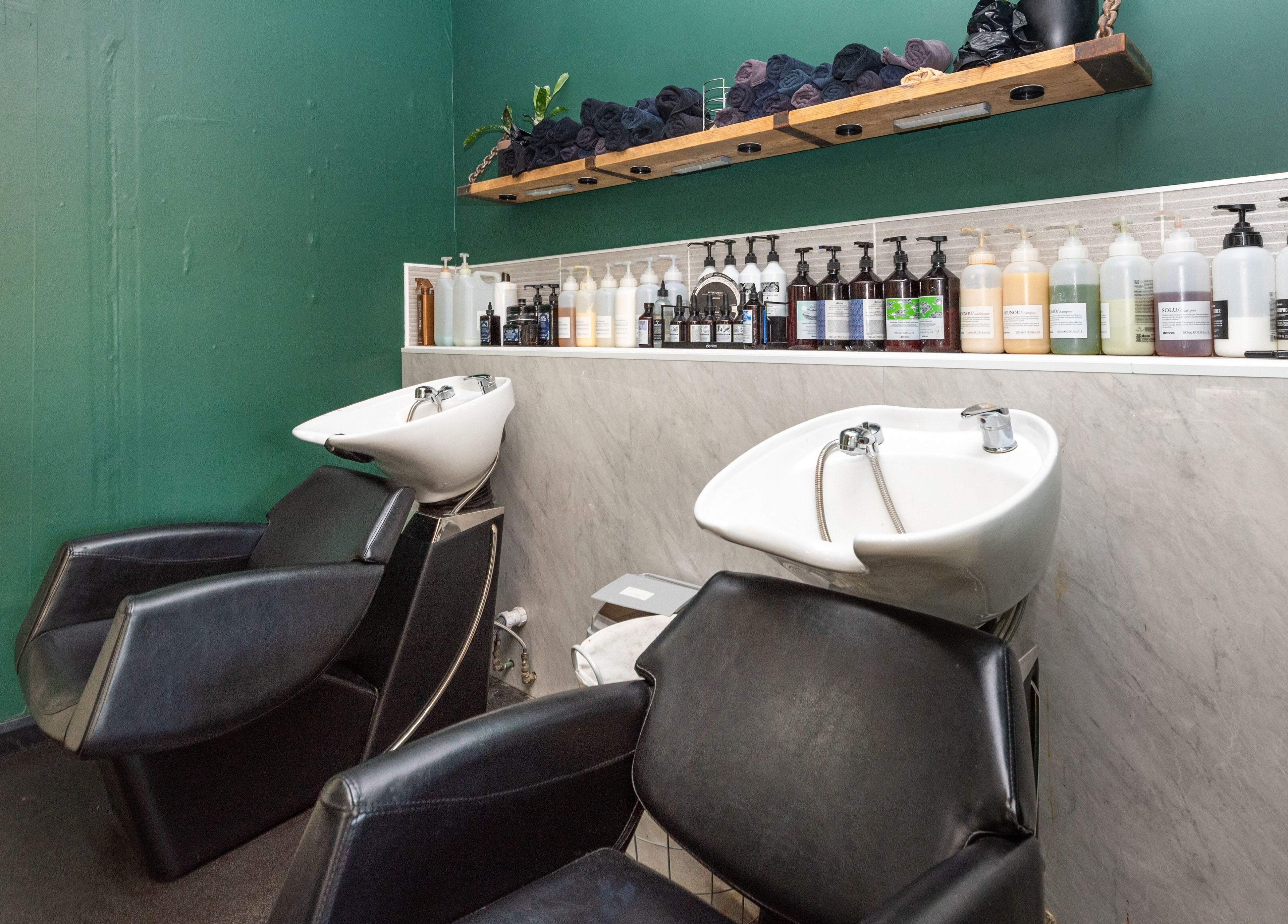 Modern wash stations at Sosta, Ash, England, GB with sleek chairs, green walls, and assorted hair products.