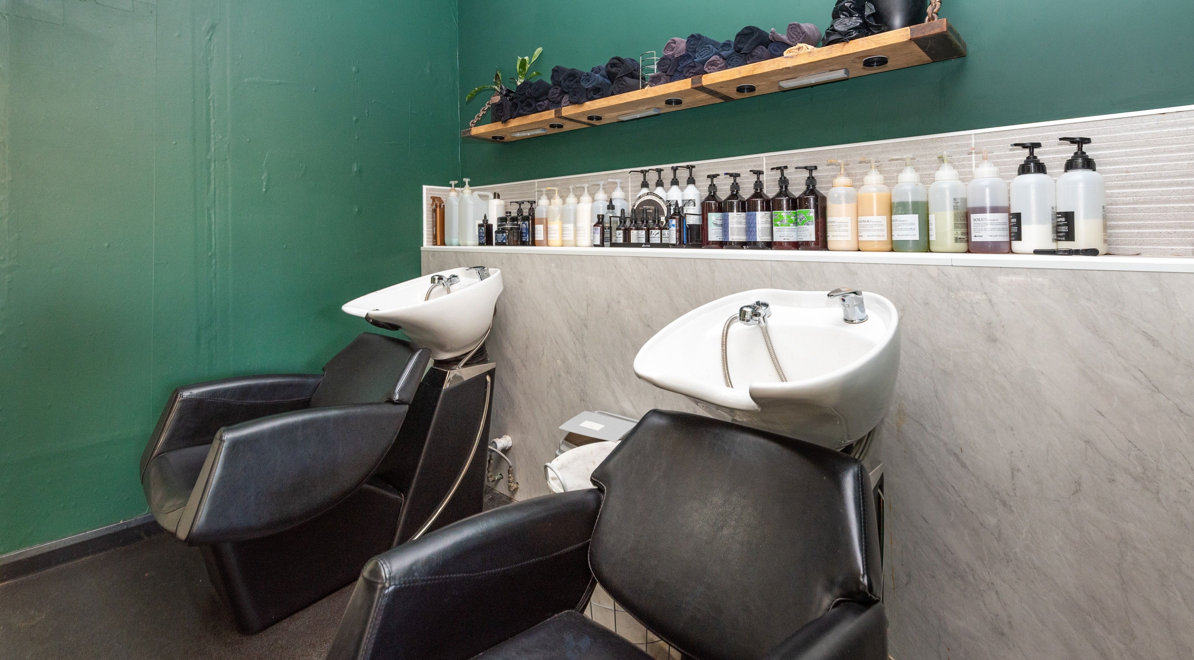 Modern wash stations at Sosta, Ash, England, GB with sleek chairs, green walls, and assorted hair products.