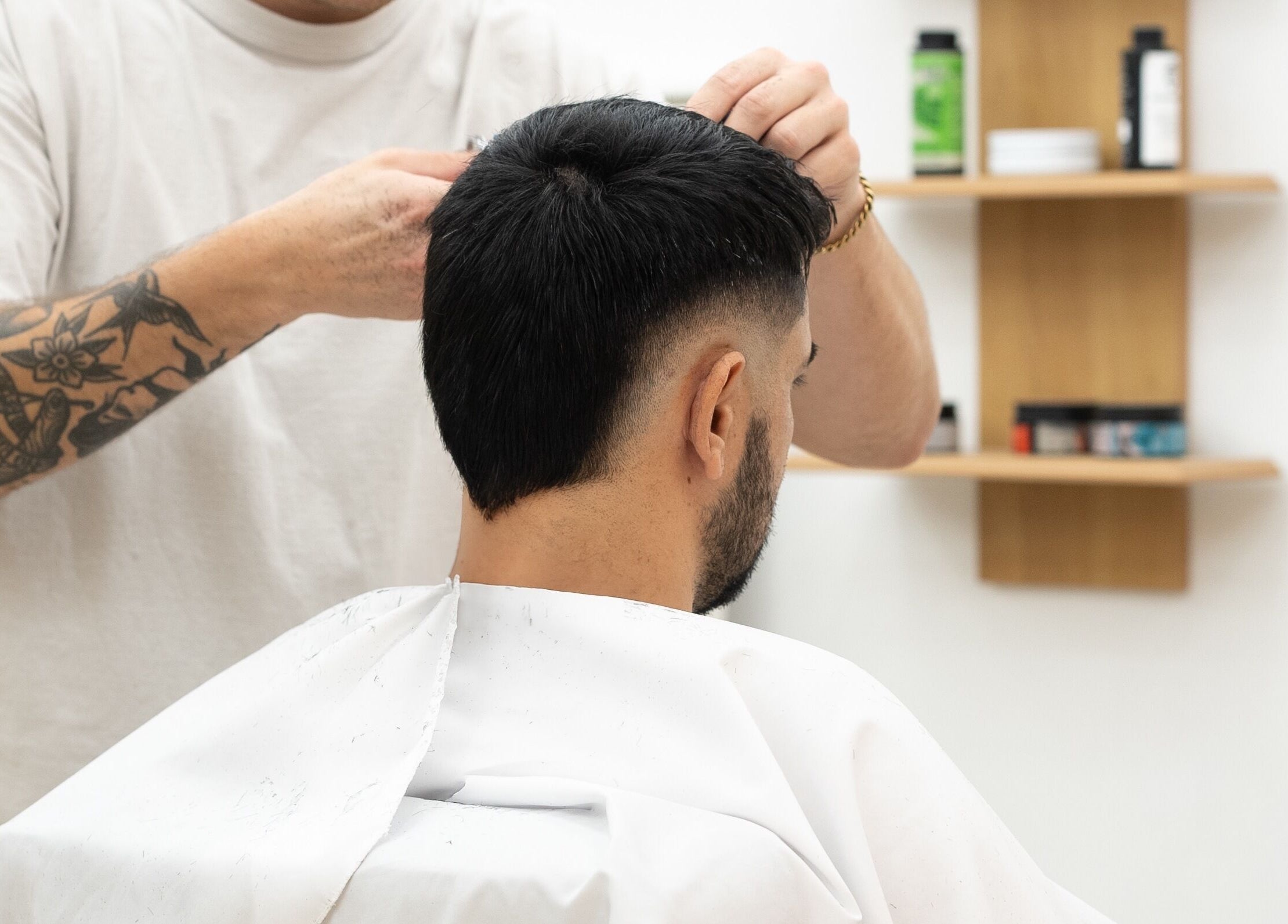 Barber styling a client's hair at ST8MNT Barbers, Gibraltar, GI. Modern interior with shelves of hair products.