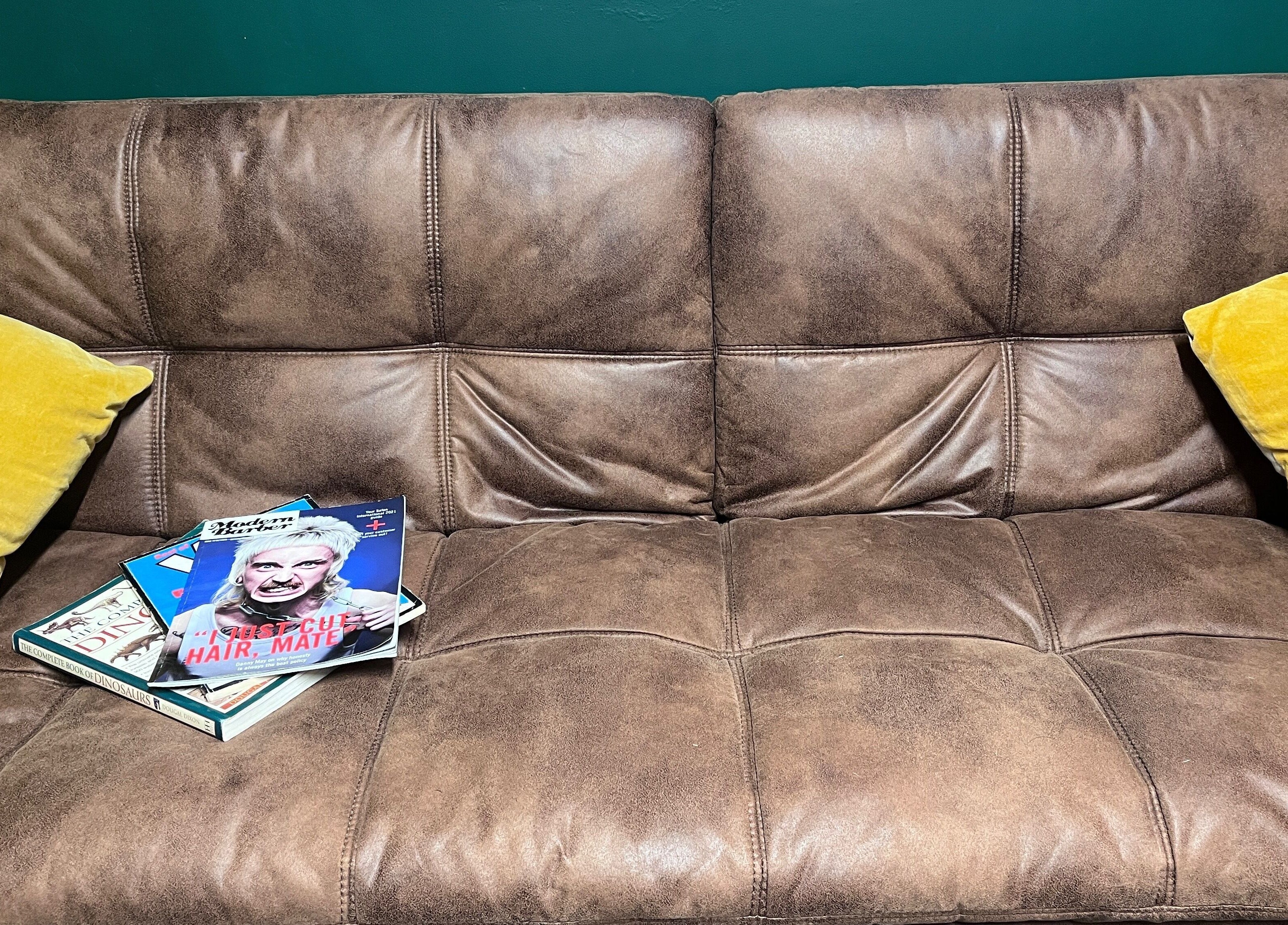 Comfy leather sofa with yellow pillows at Cabin Barbers, Chessington, England, GB.