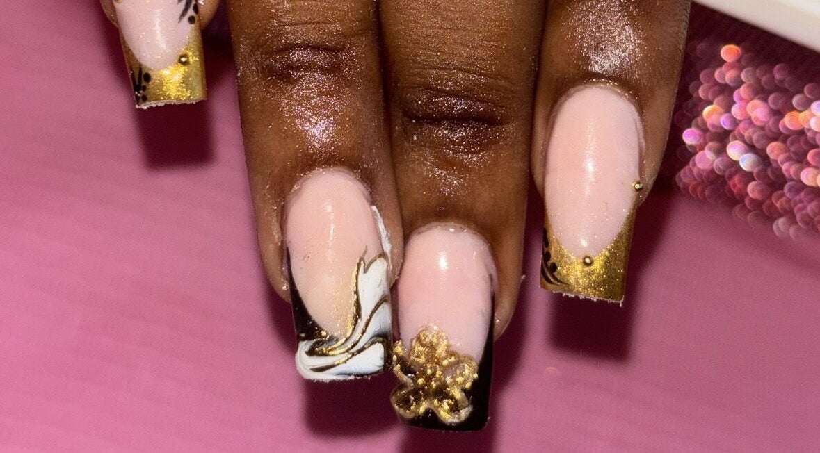 Elegant gold-accented nail art by SquaredByT in Cole Bay, Sint Maarten, SX, set against a pink backdrop.
