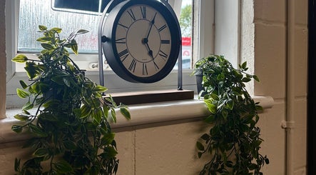 Elegant clock and lush plants on a window sill at A.J.Healing, South Ockendon, England, GB.
