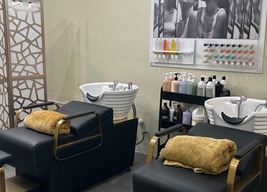 Zona de lavado elegante en Natalia Nieves Salon, Caguas, Caguas, PR, con sillas de lujo y productos para el cuidado.