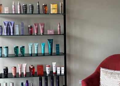 Estante de productos de belleza en Natalia Nieves Salon, Caguas, Caguas, PR junto a una silla roja cómoda.