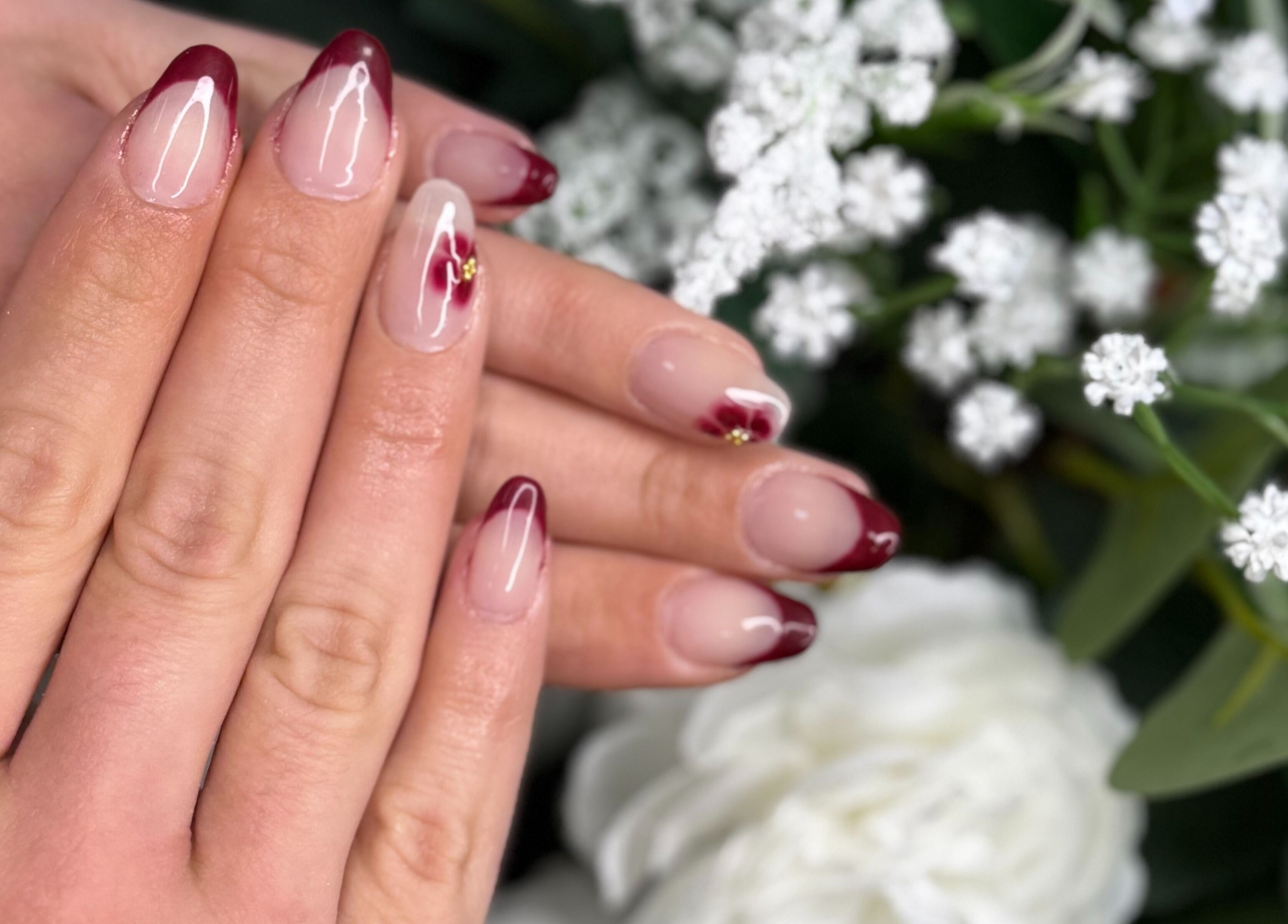 Dainty red-tipped nails at Magnolia Beauty Bar, Mildura, Victoria, AU surrounded by white flowers.