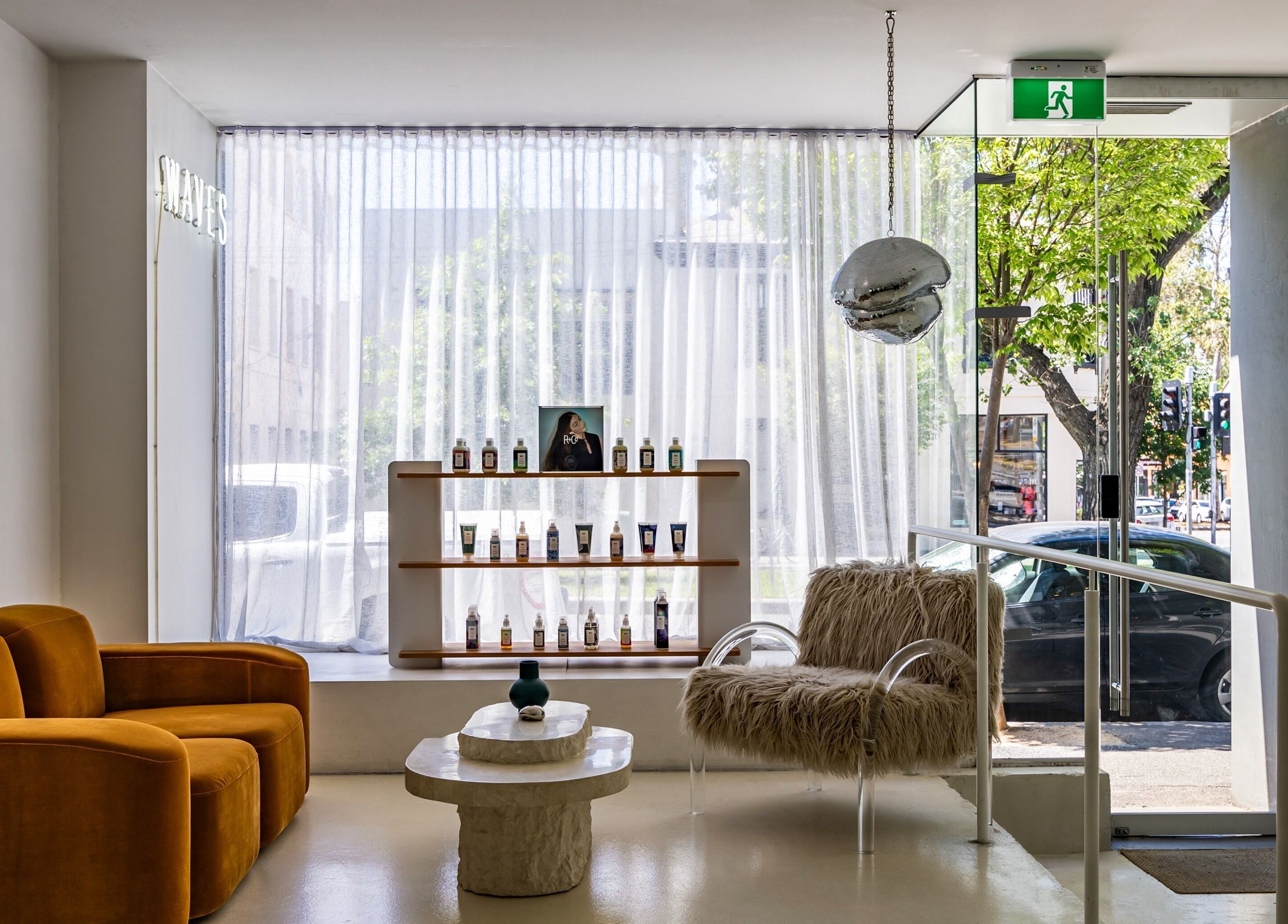 Cozy lobby at WAVES in Melbourne, Victoria, AU with modern decor, velvet sofas, and beauty products on display.