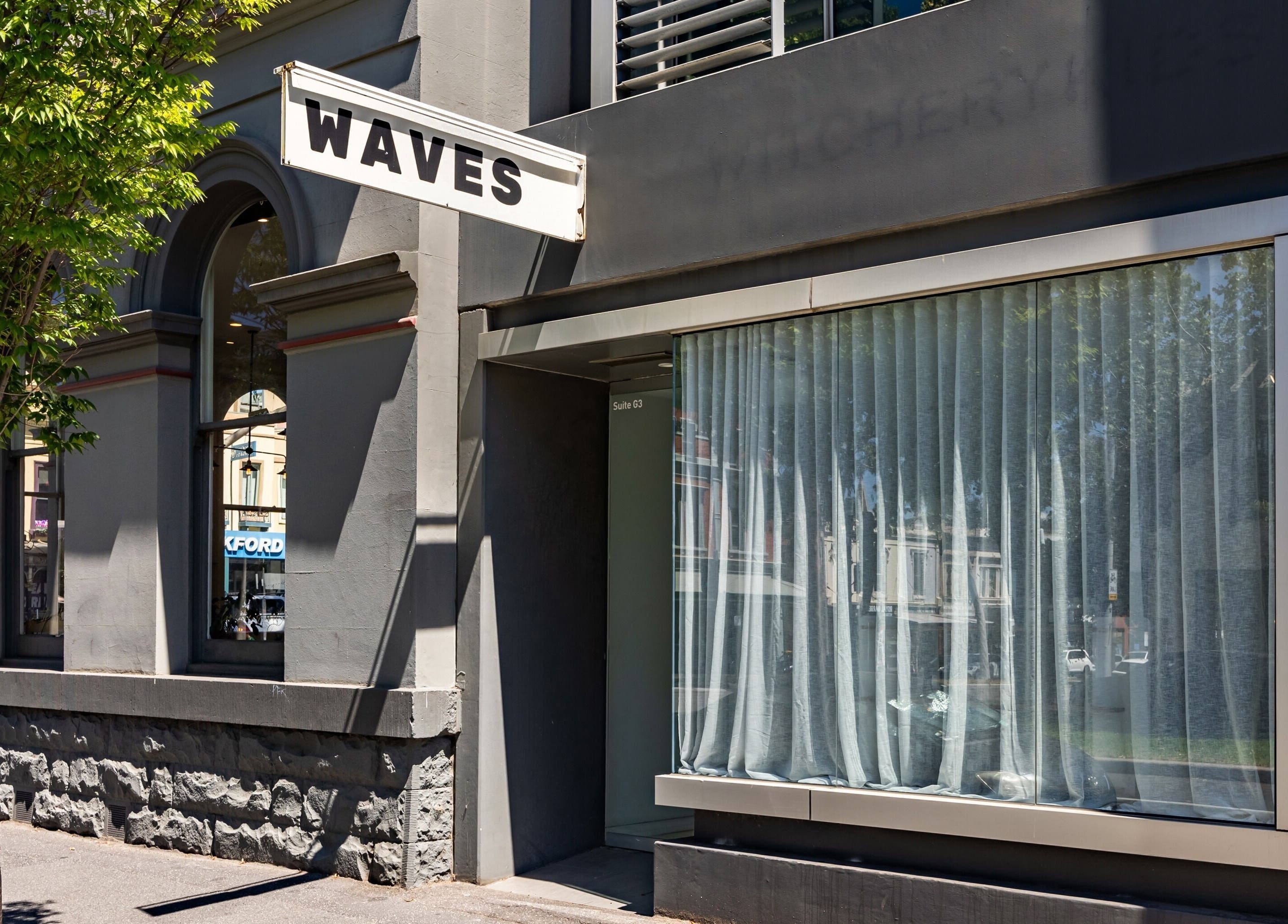 Exterior of WAVES beauty and wellness venue in Melbourne, Victoria, AU with modern gray facade and signage.