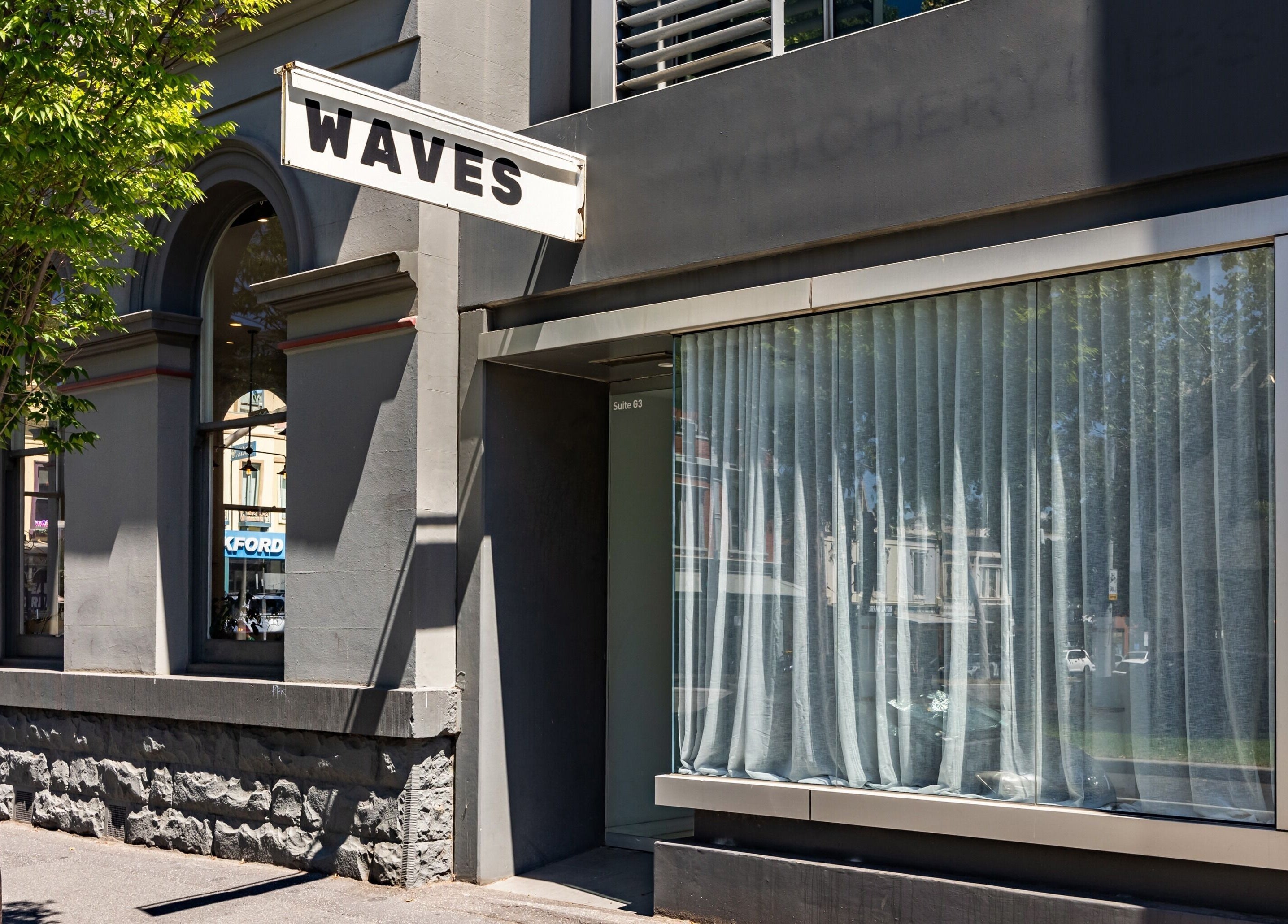 Exterior of WAVES beauty and wellness venue in Melbourne, Victoria, AU with modern gray facade and signage.