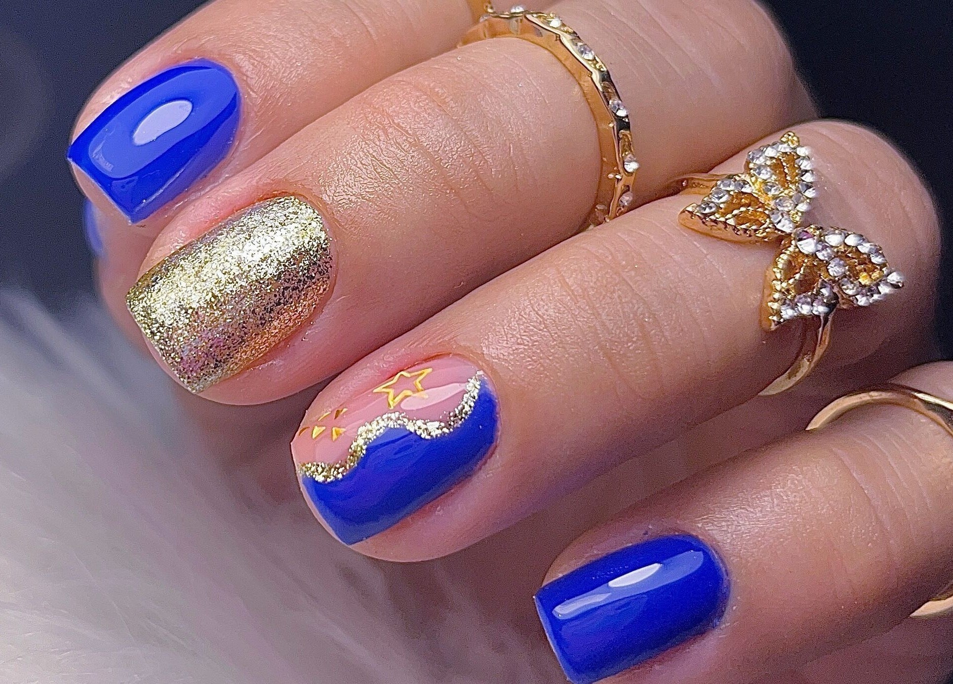 Elegante manicura azul-oro de Yoss Nails en Memphis, Tennessee, US. Destacan brillantes y detalles creativos.