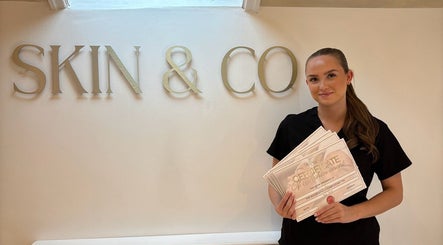 Staff member at 27Skin in Lingfield, England, holds achievement certificates with pride.