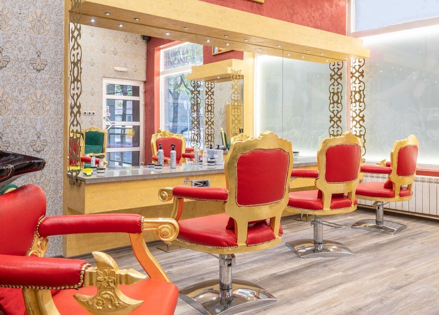 Luxurious interior of Raskoljnikov Beauty Studio in Београд, RS, featuring opulent red and gold styling chairs.
