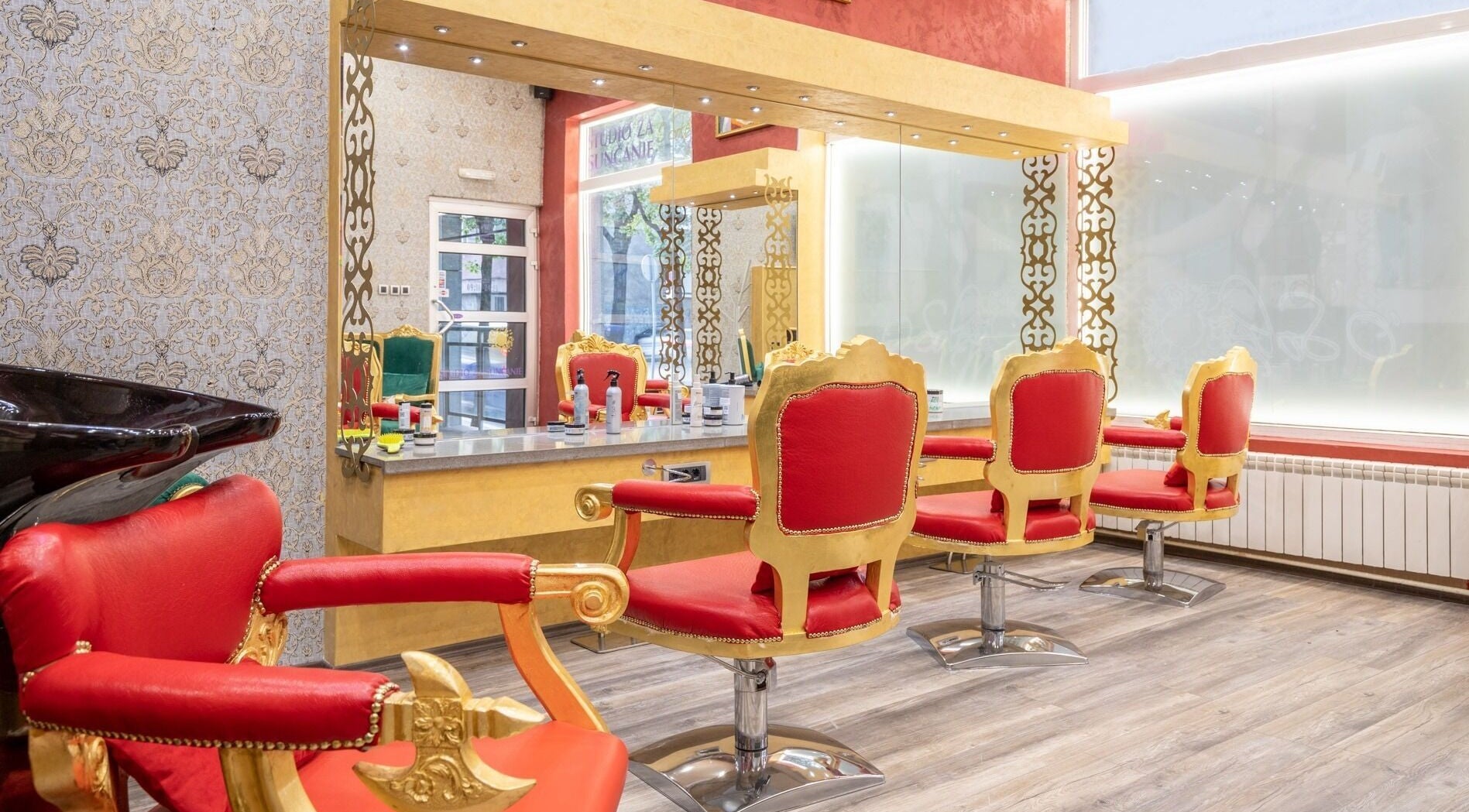 Luxurious interior of Raskoljnikov Beauty Studio in Београд, RS, featuring opulent red and gold styling chairs.