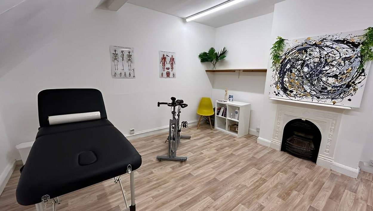 First Place Physiotherapy room in Fleet, England, GB featuring a massage bed, exercise bike, and modern art.
