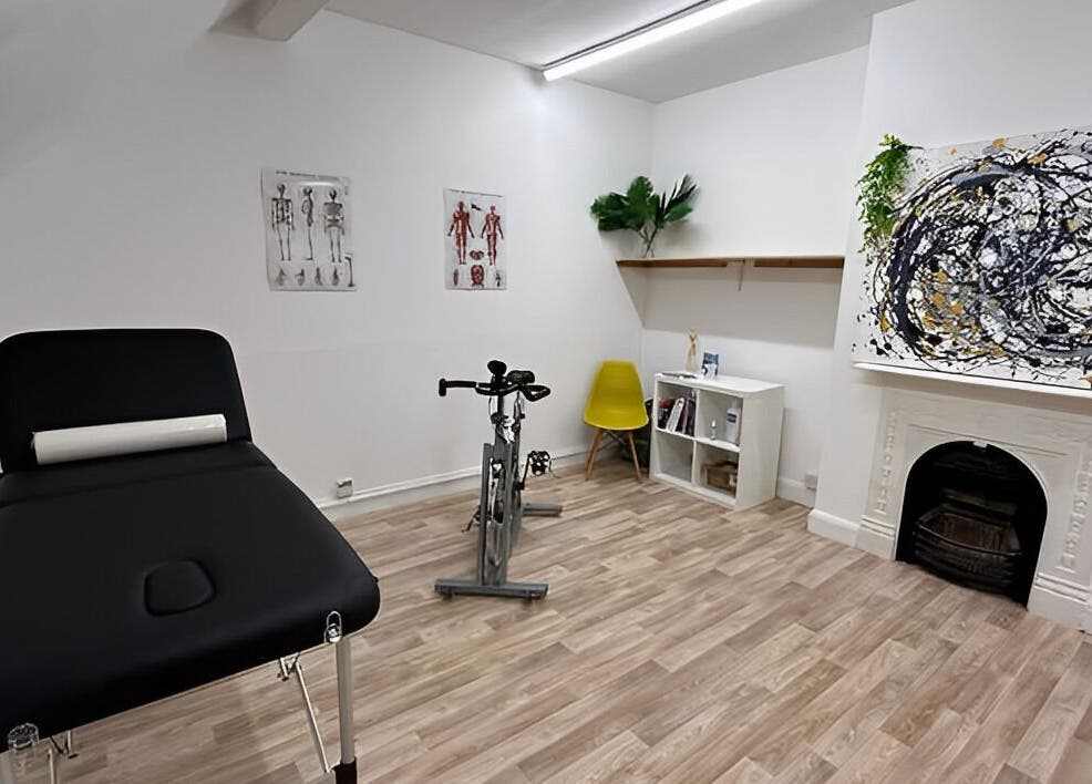 First Place Physiotherapy room in Fleet, England, GB featuring a massage bed, exercise bike, and modern art.
