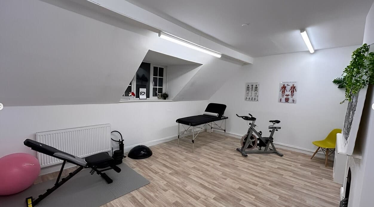 Modern therapy room at First Place Physiotherapy in Fleet, England, with gym equipment and treatment bed.