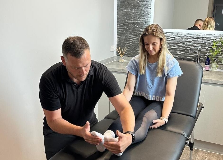 A physiotherapist at First Place Physiotherapy, Fleet, England, GB helps a client with leg therapy.