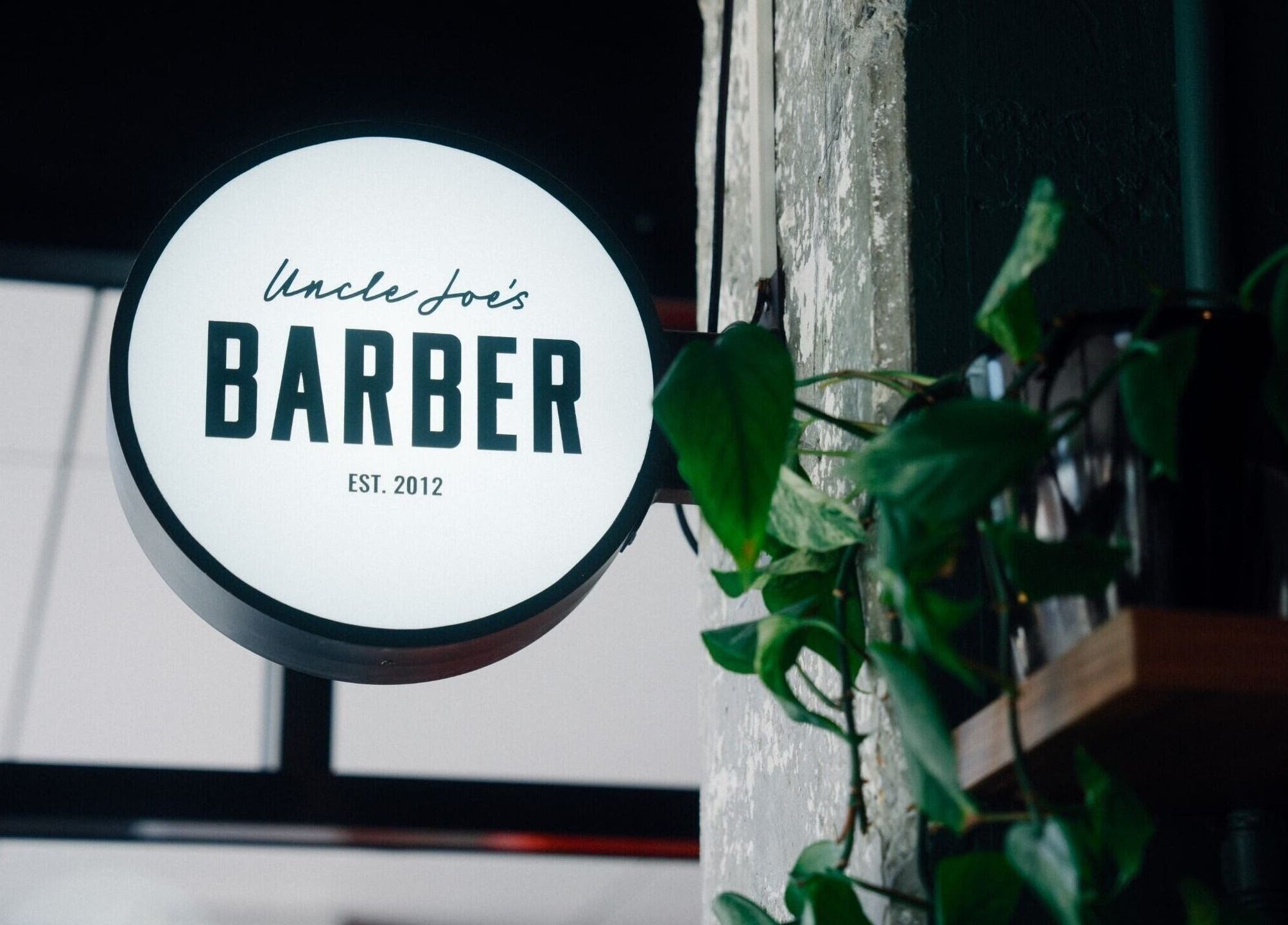 Illuminated sign of Uncle Joes Barber - Fremantle, nestled in greenery, Fremantle, Western Australia, AU.