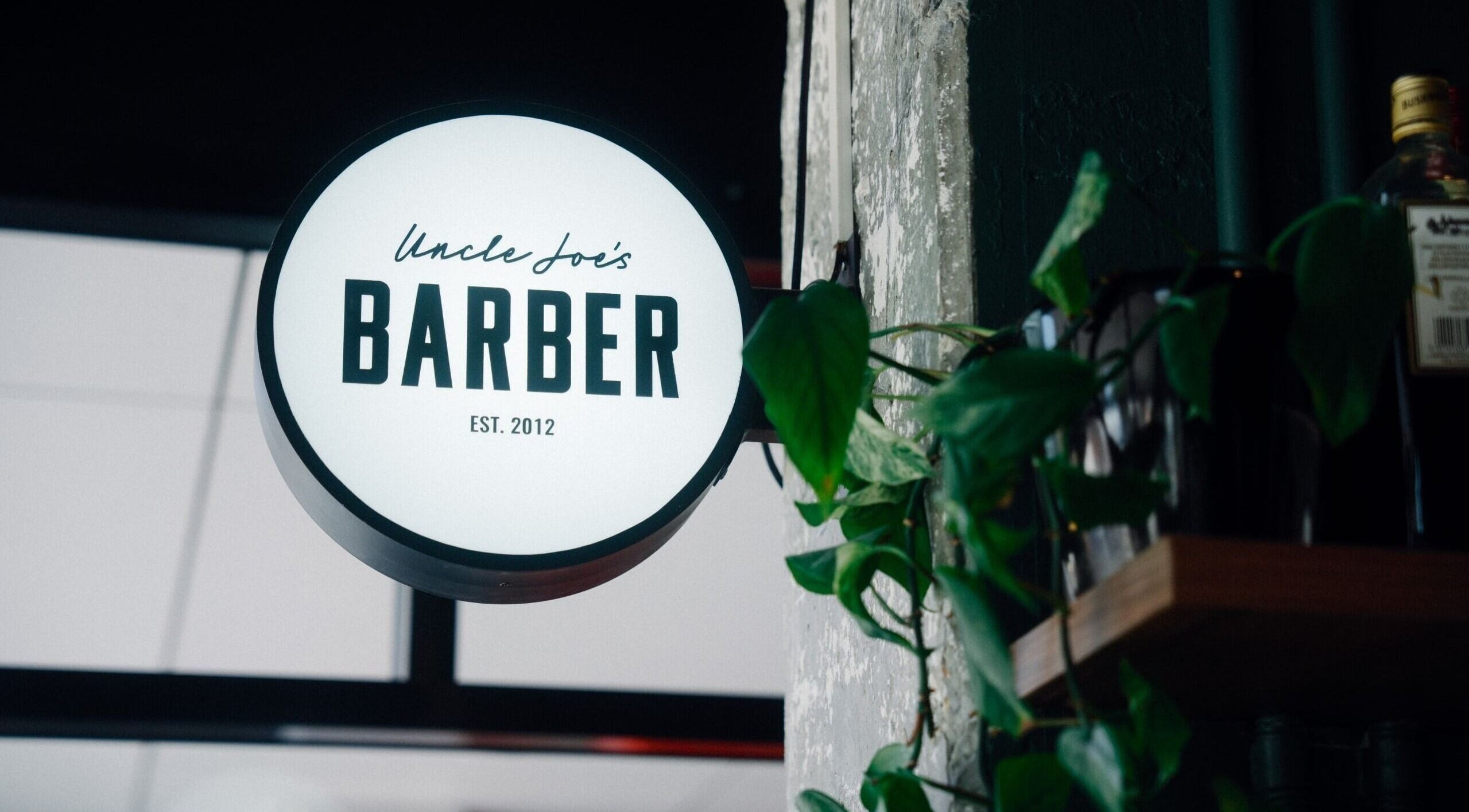Illuminated sign of Uncle Joes Barber - Fremantle, nestled in greenery, Fremantle, Western Australia, AU.