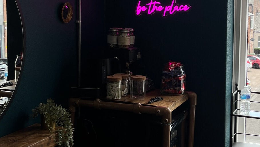 Chic neon-lit interior at Sacred Hair, North Shields, England. Aesthetic wooden counter with jars and decor.