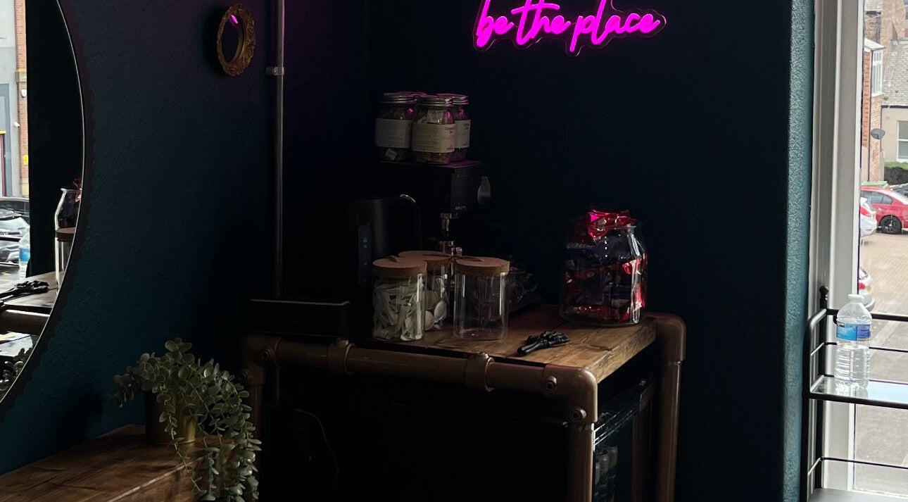 Chic neon-lit interior at Sacred Hair, North Shields, England. Aesthetic wooden counter with jars and decor.