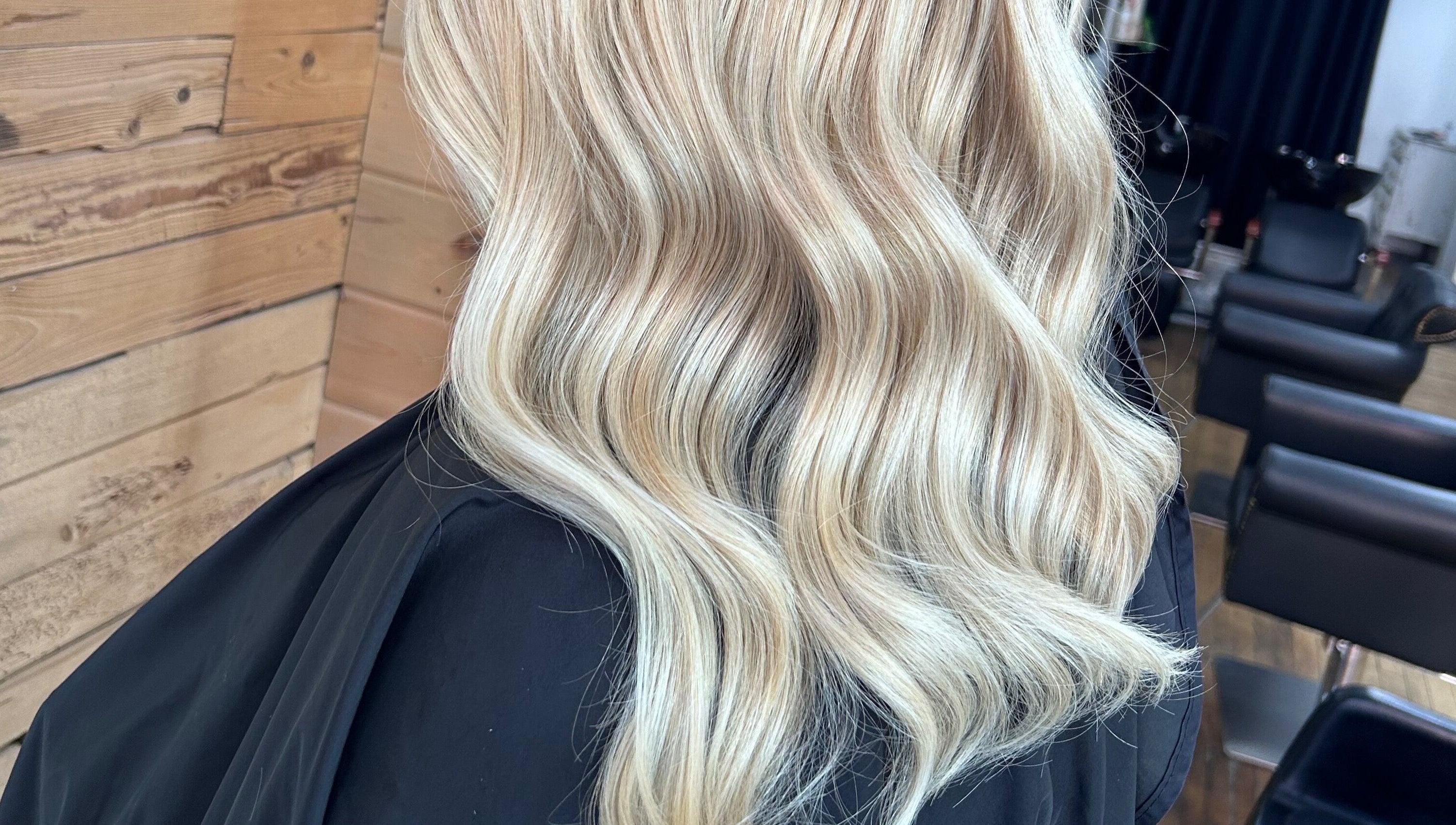 Blonde wavy hairstyle styled at Meg's Studio, Orillia, Ontario, CA with wooden backdrop and salon chairs.