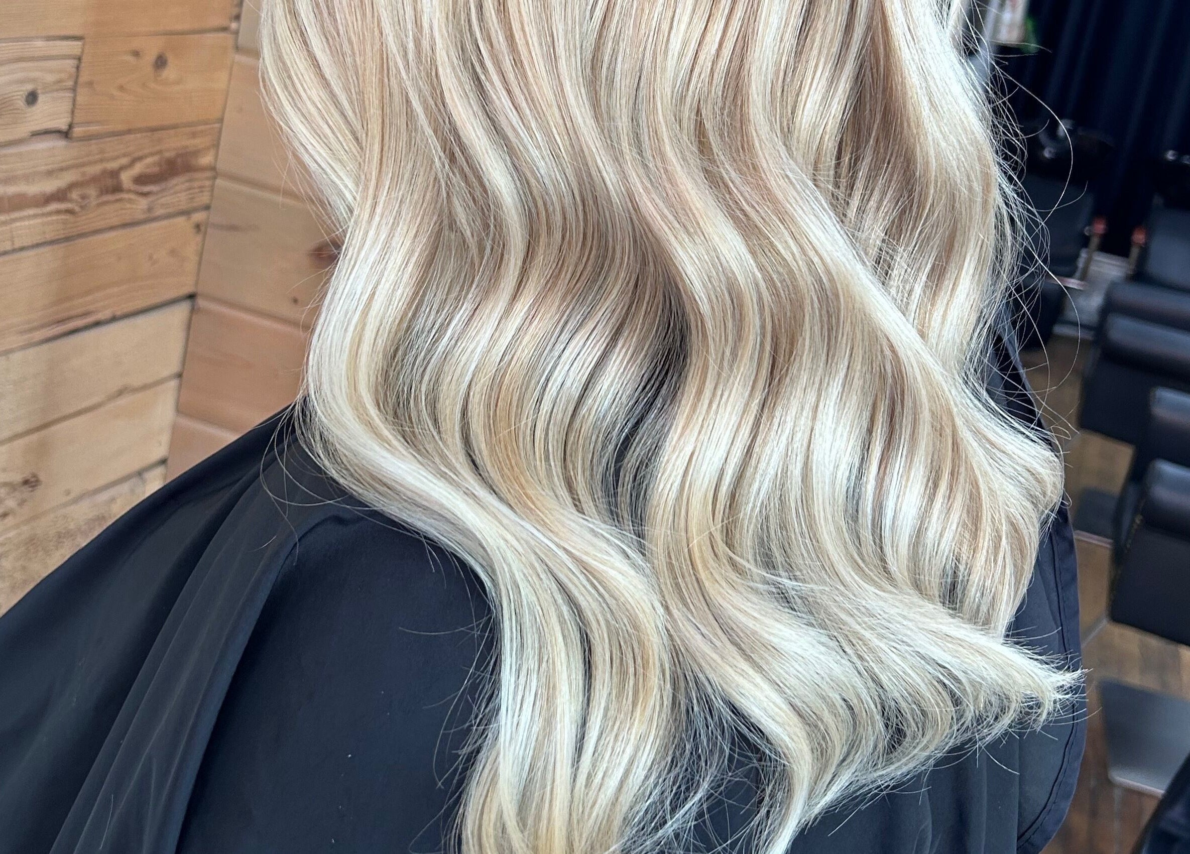Blonde wavy hairstyle styled at Meg's Studio, Orillia, Ontario, CA with wooden backdrop and salon chairs.