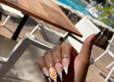 Hand with floral nail art at Nailuxebytasha, Willemstad, CW, showcasing elegant manicure in sunny setting.