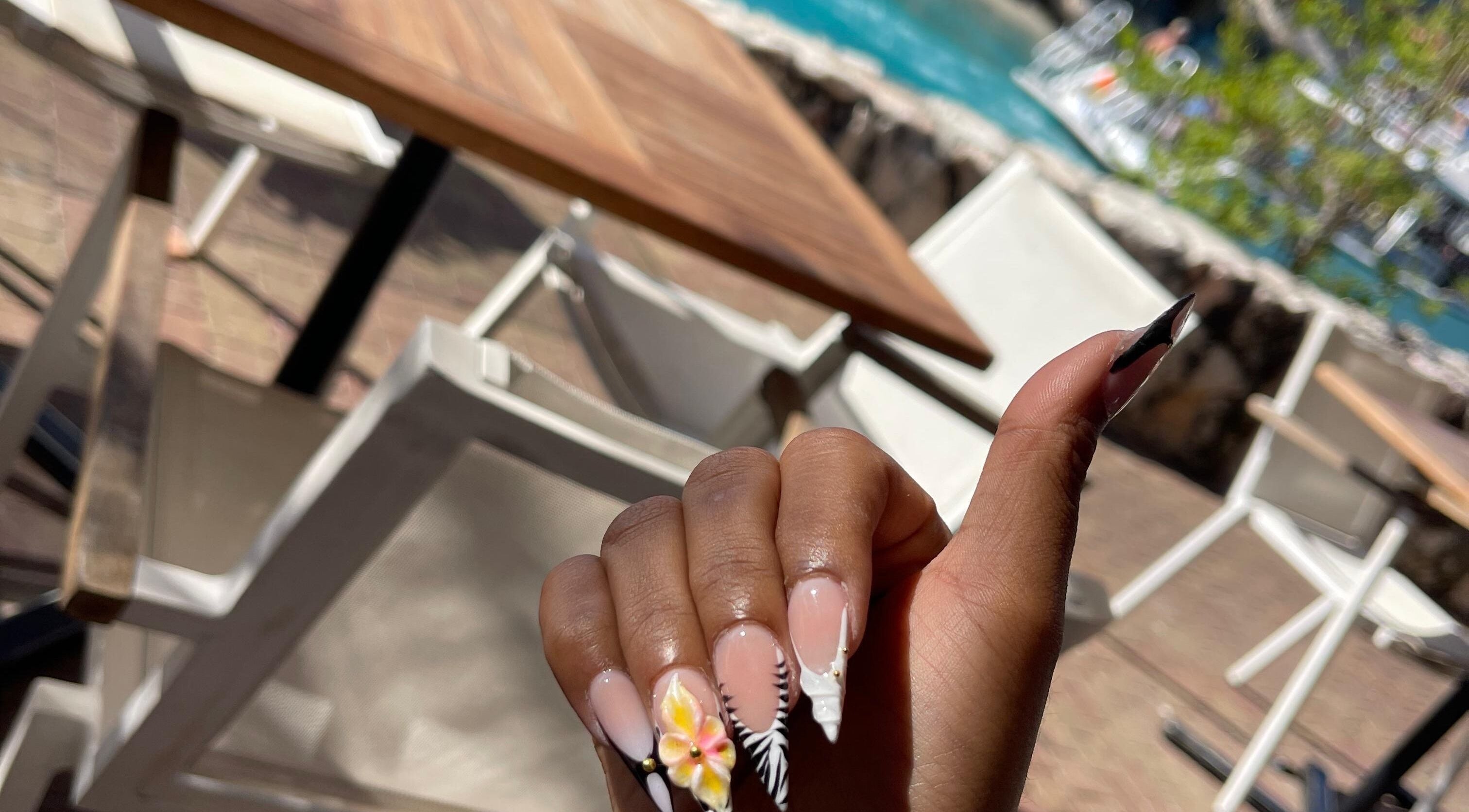 Hand with floral nail art at Nailuxebytasha, Willemstad, CW, showcasing elegant manicure in sunny setting.